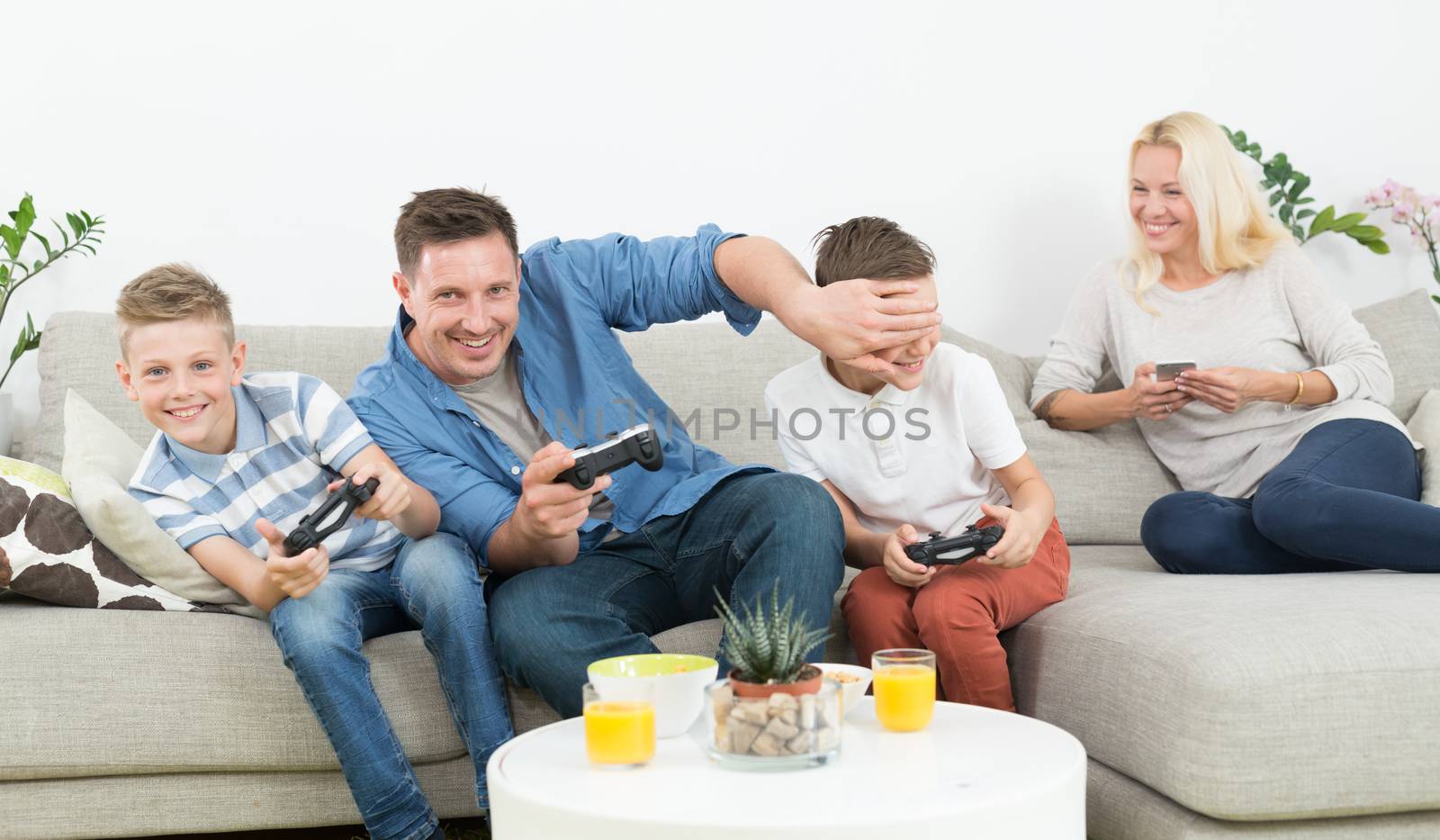 Happy young family playing videogame console on TV. Spending quality leisure time with children and family concept. Gaming consoles are generic and debranded.