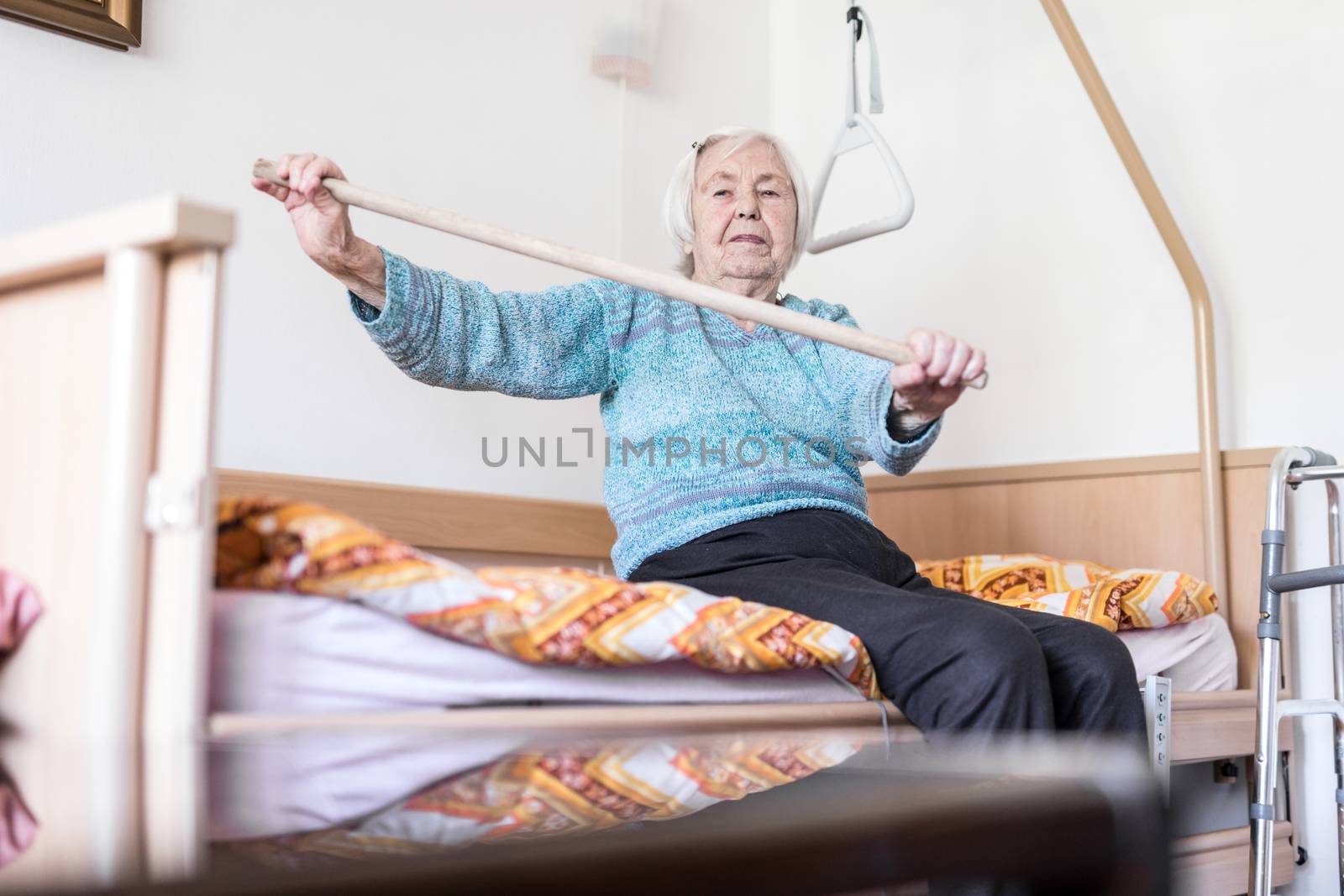 Elderly 96 years old woman exercising with a stick sitting on her bad. Geriatric health care home assisted support for older people concept. Care for the elderly.
