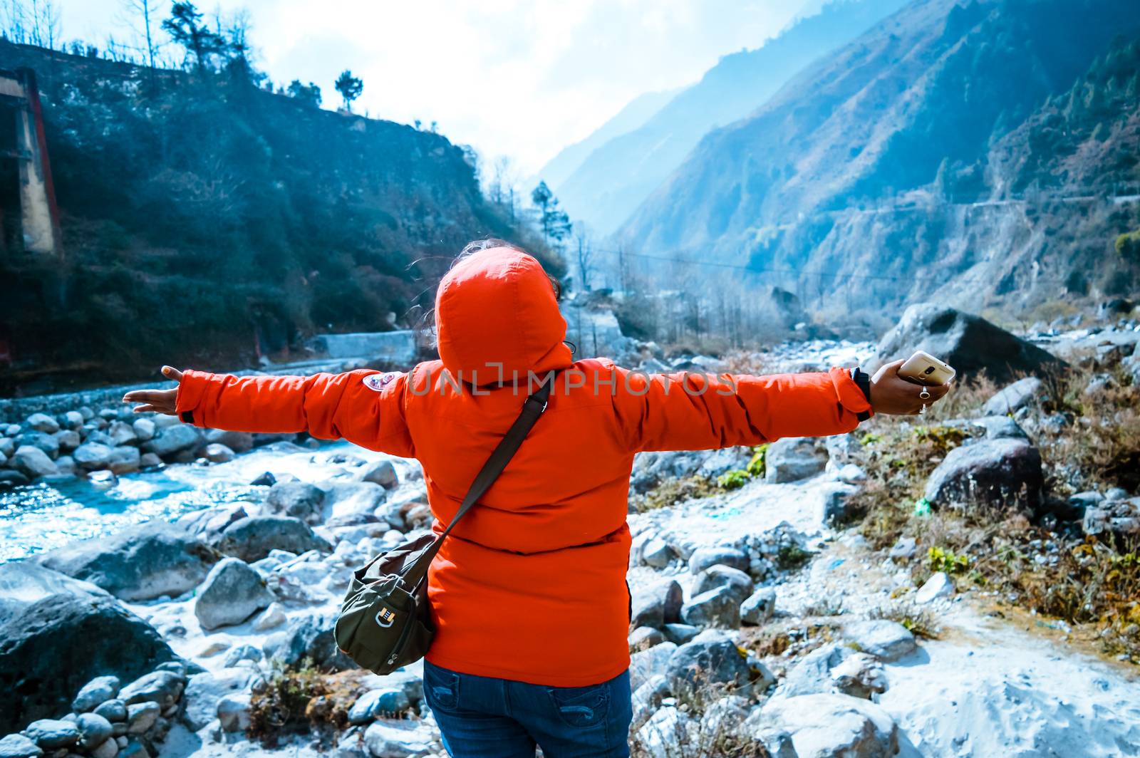 On edge of a himalayan rocky cliff an nomadic woman stretched her hands to heaven as a sign of freedom or victory. A fantastic himalayan valley in front. Concept of breathing, journey, life and love.