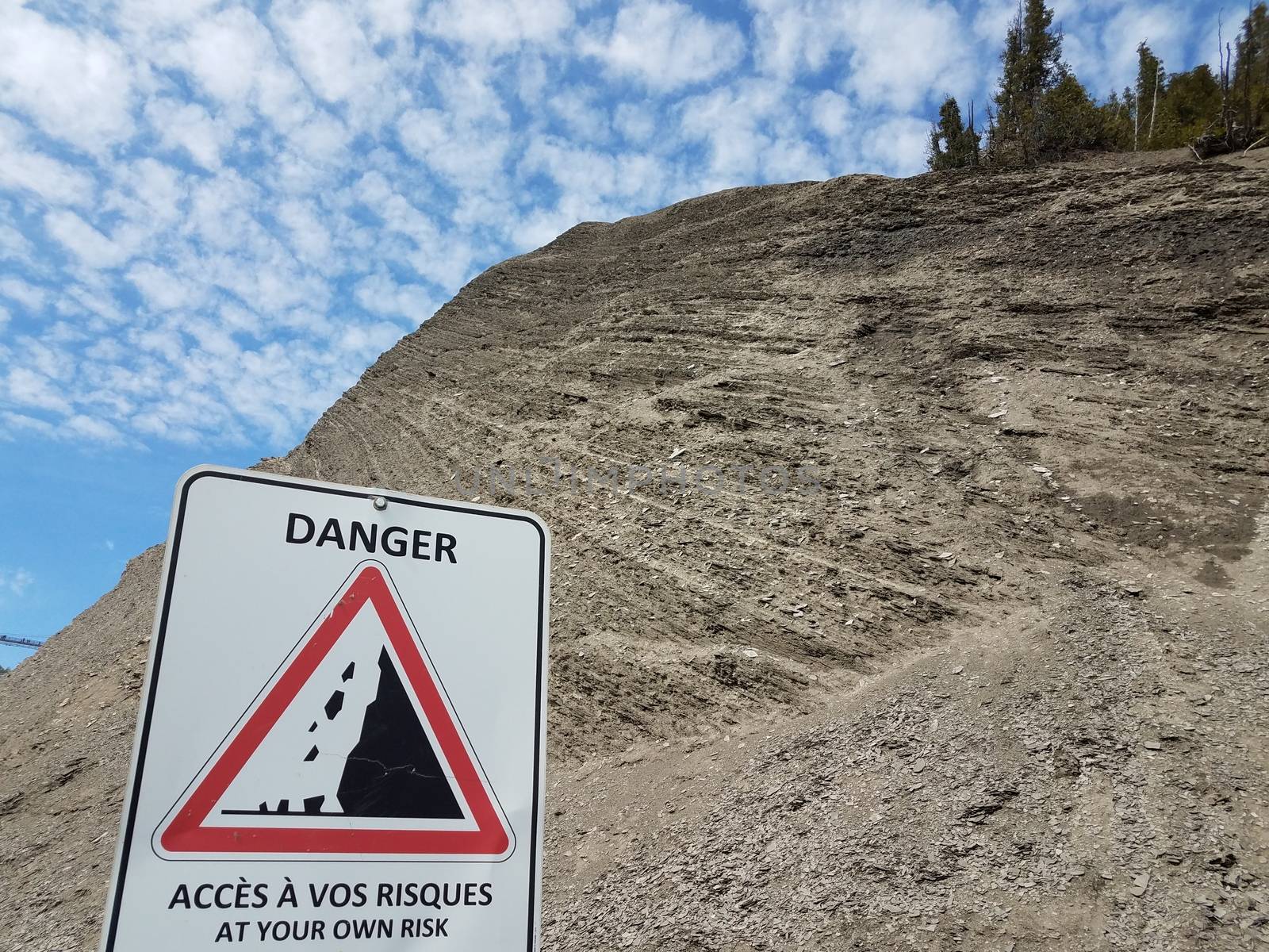 tall rocky mountain or hill with danger at your own risk sign in English and French