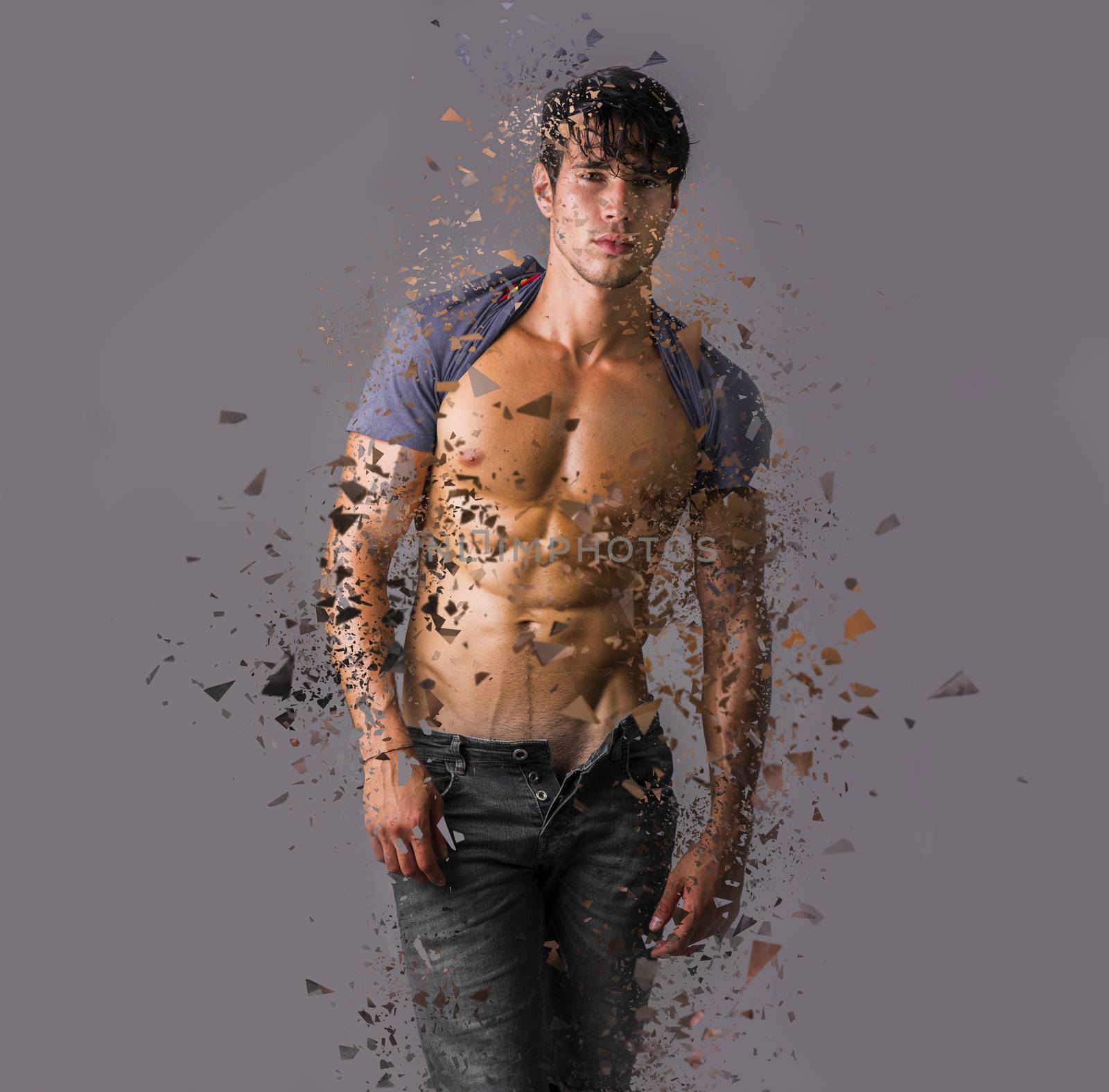 Handsome man with muscular torso standing on gray background in dispersion looking at camera