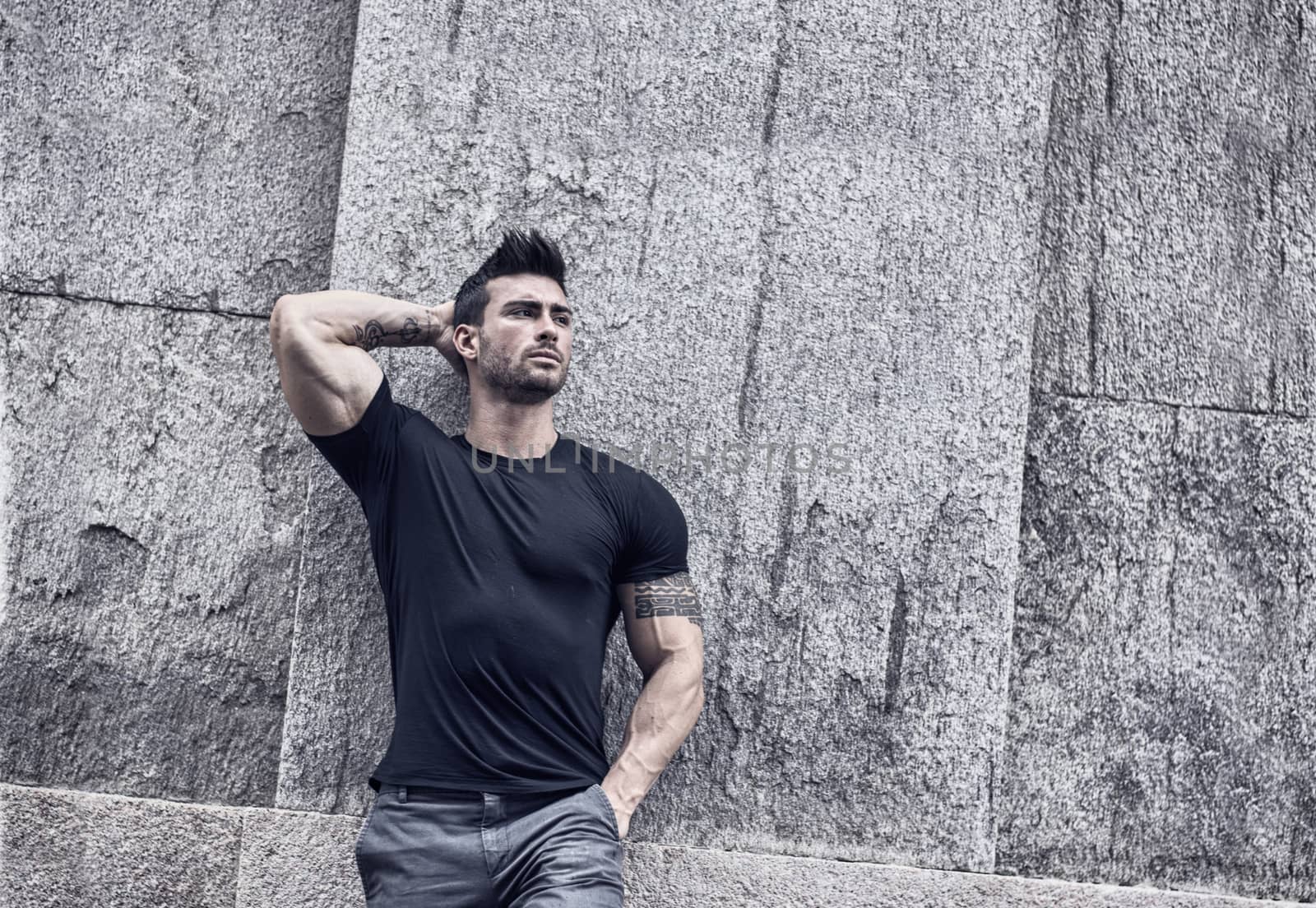 Attractive man outdoor. Athletic build, with tight t-shirt, leaning against stone wall