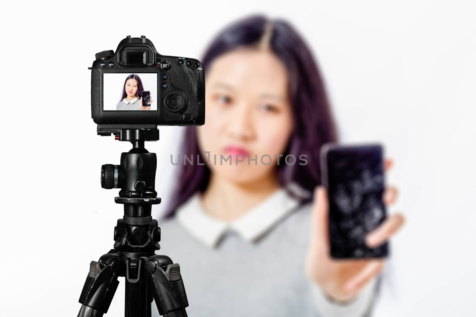 Focus on live view on camera on tripod, teenage girl  holds cracked phone image on back screen with blurred scene in background. Teenage vlogger livestreaming show concept