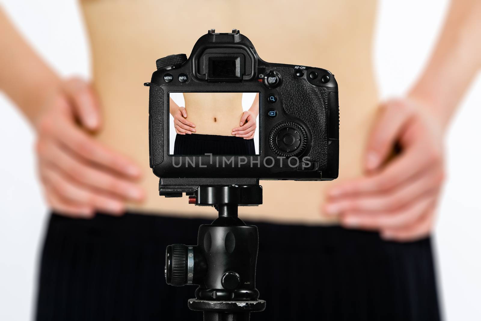 Focus on live view on camera on tripod, teenage girl  showing waistline from diet image on back screen with blurred scene in background. Teenage vlogger livestreaming show concept