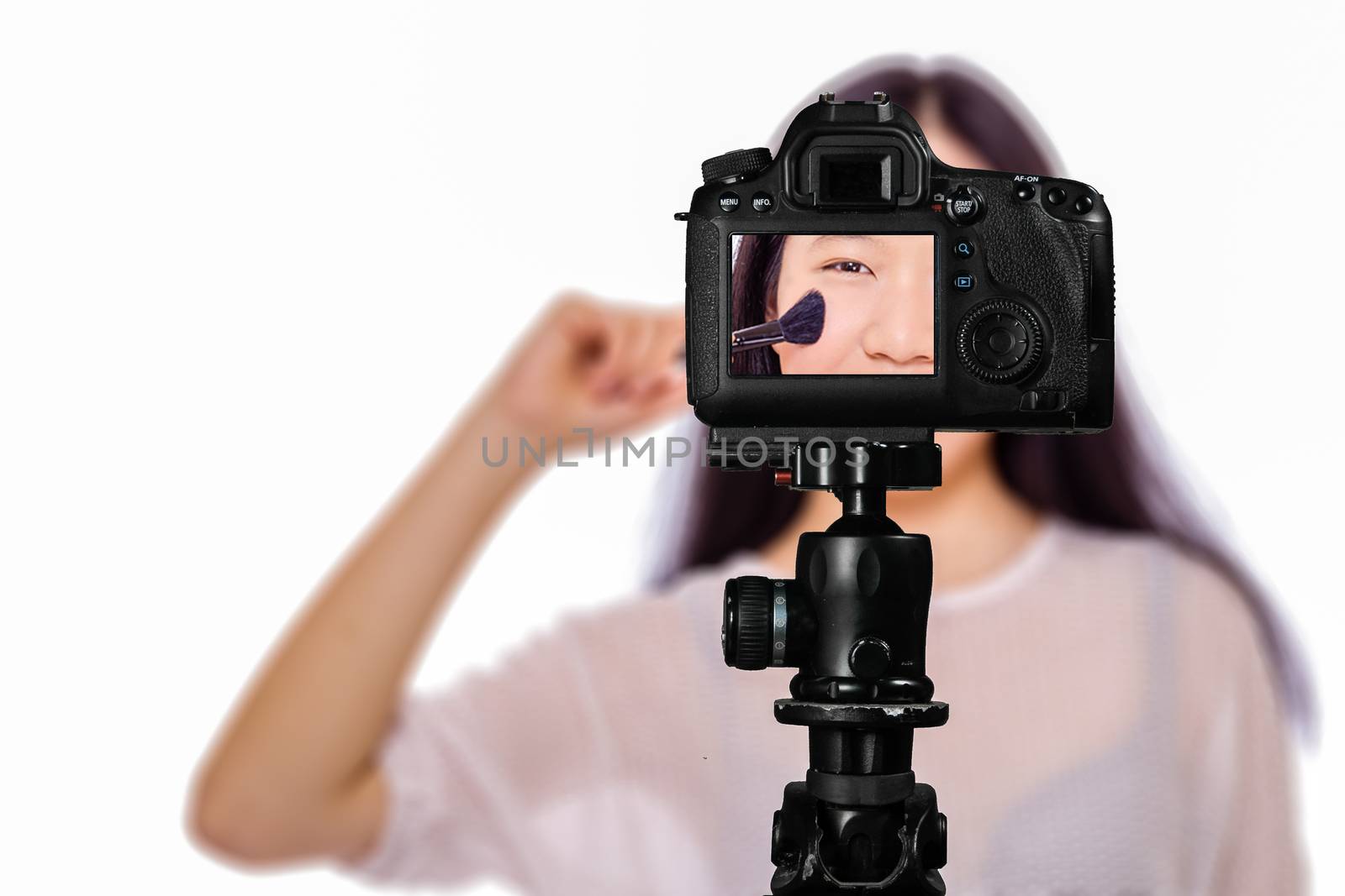 Focus on live view on camera on tripod, teenage girl  using cosmetics image on back screen with blurred scene in background. Teenage vlogger livestreaming show concept