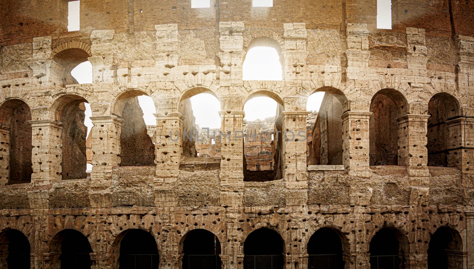 the Colosseum of Rome during sunset with sun rays filtering through the arches