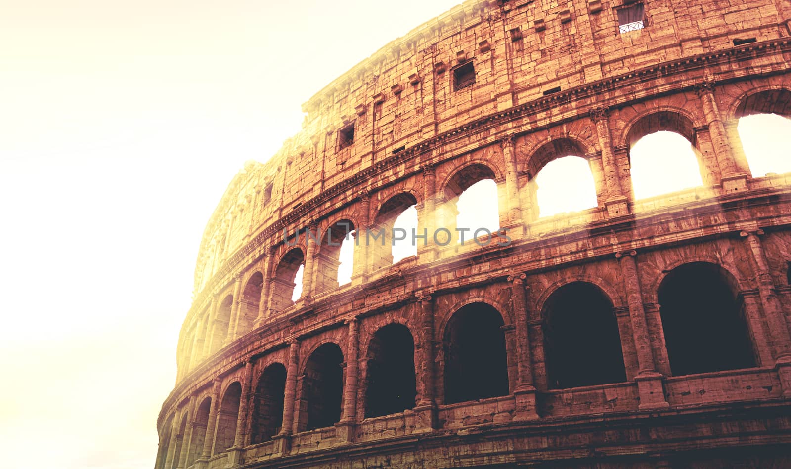 dramatic image of the Colosseum of Rome during sunset with sun rays filtering through the arches