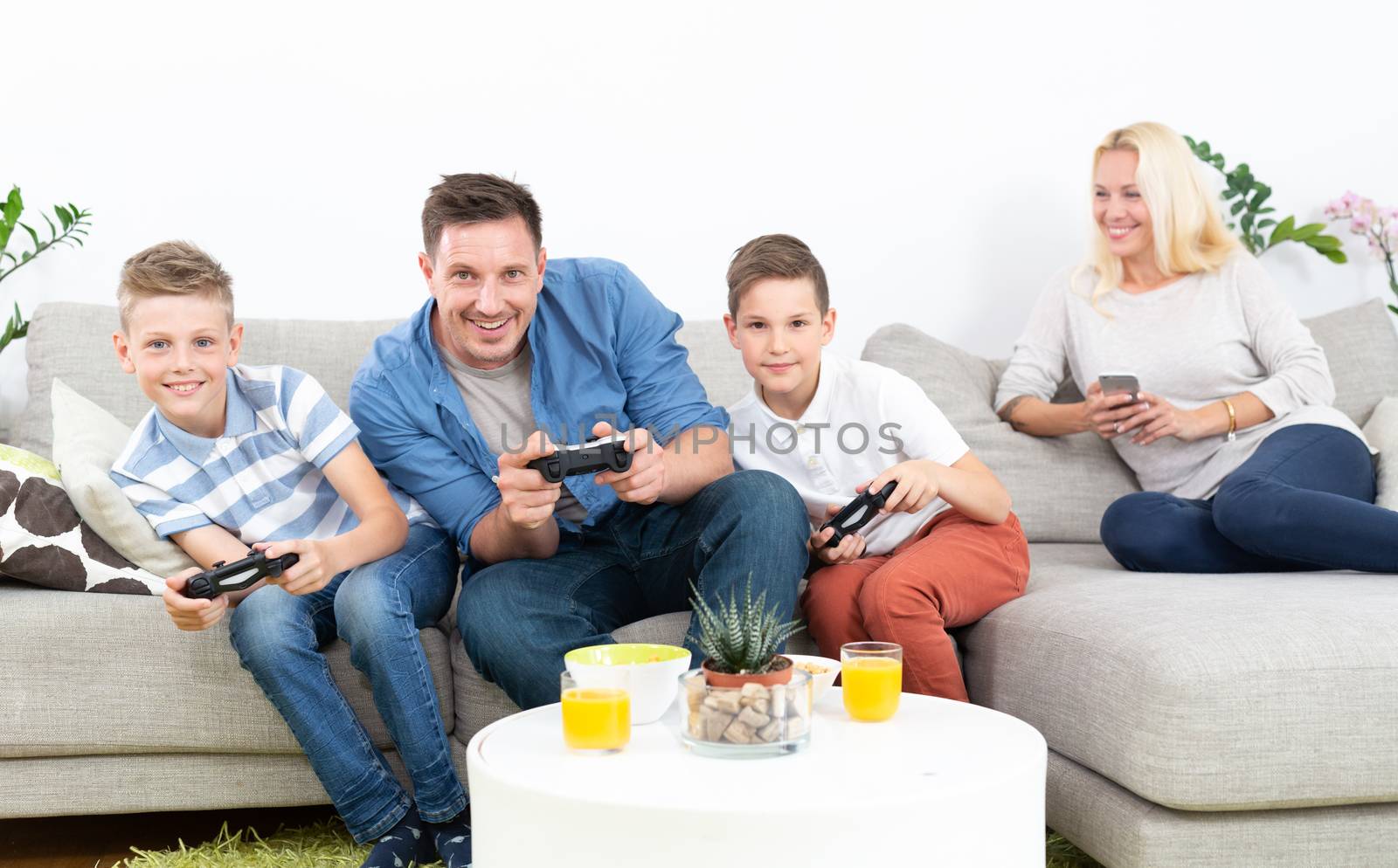 Happy young family playing videogame console on TV. Spending quality leisure time with children and family concept. Gaming consoles are generic and debranded.