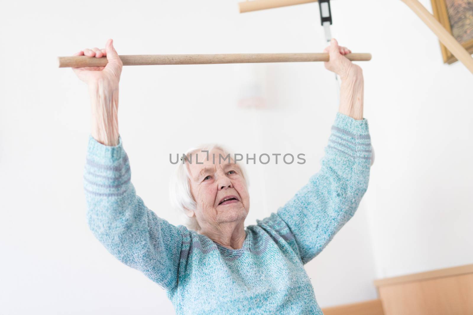 Elderly 96 years old woman exercising with a stick sitting on her bad. Geriatric health care home assisted support for older people concept. Care for the elderly.