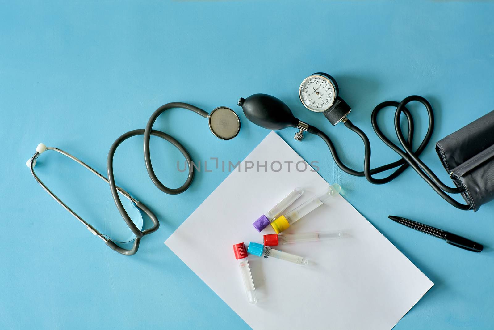 White sheet paper with black pen and phonendoscope stethoscope, sphygmomanometer, vacuum venipuncture test tubes on blue background with copy space for text. Medicine consept.