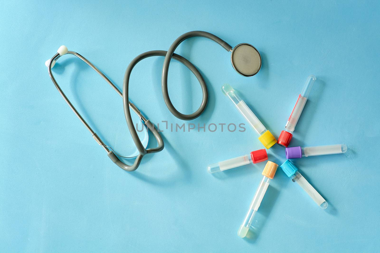 Phonendoscope stethoscope, different colored empty vacuum venipuncture test tubes on blue background with copy space for text. Medicine consept.