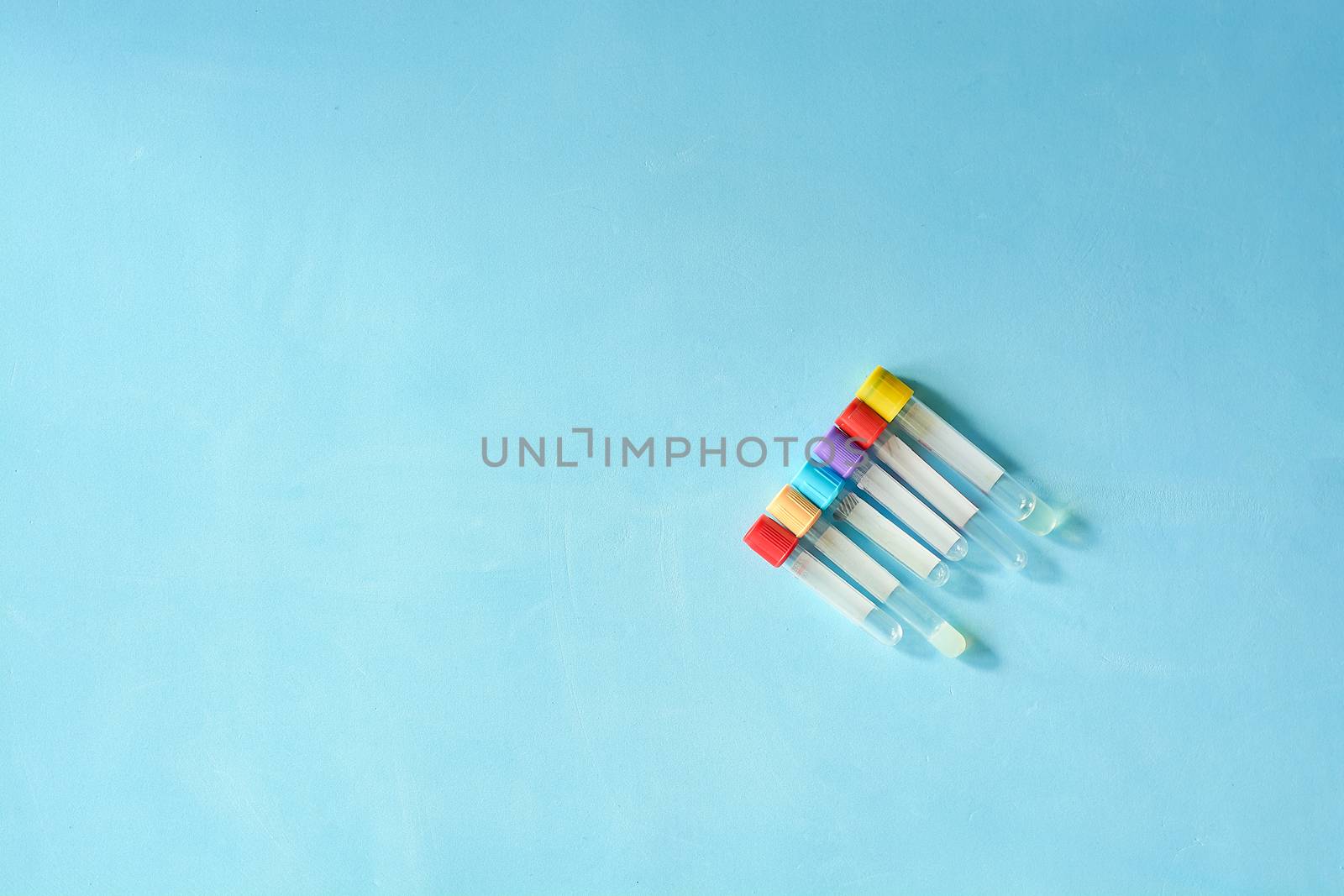 Different color and size empty vacuum venipuncture test tubes on blue background with copy space for text. Health life medicine concept.