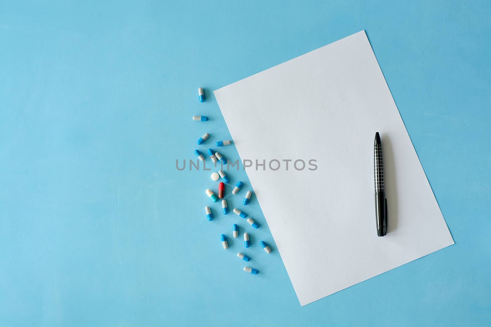 White sheet paper with black pen and colored different pills, capsules on blue background. by nixrenas