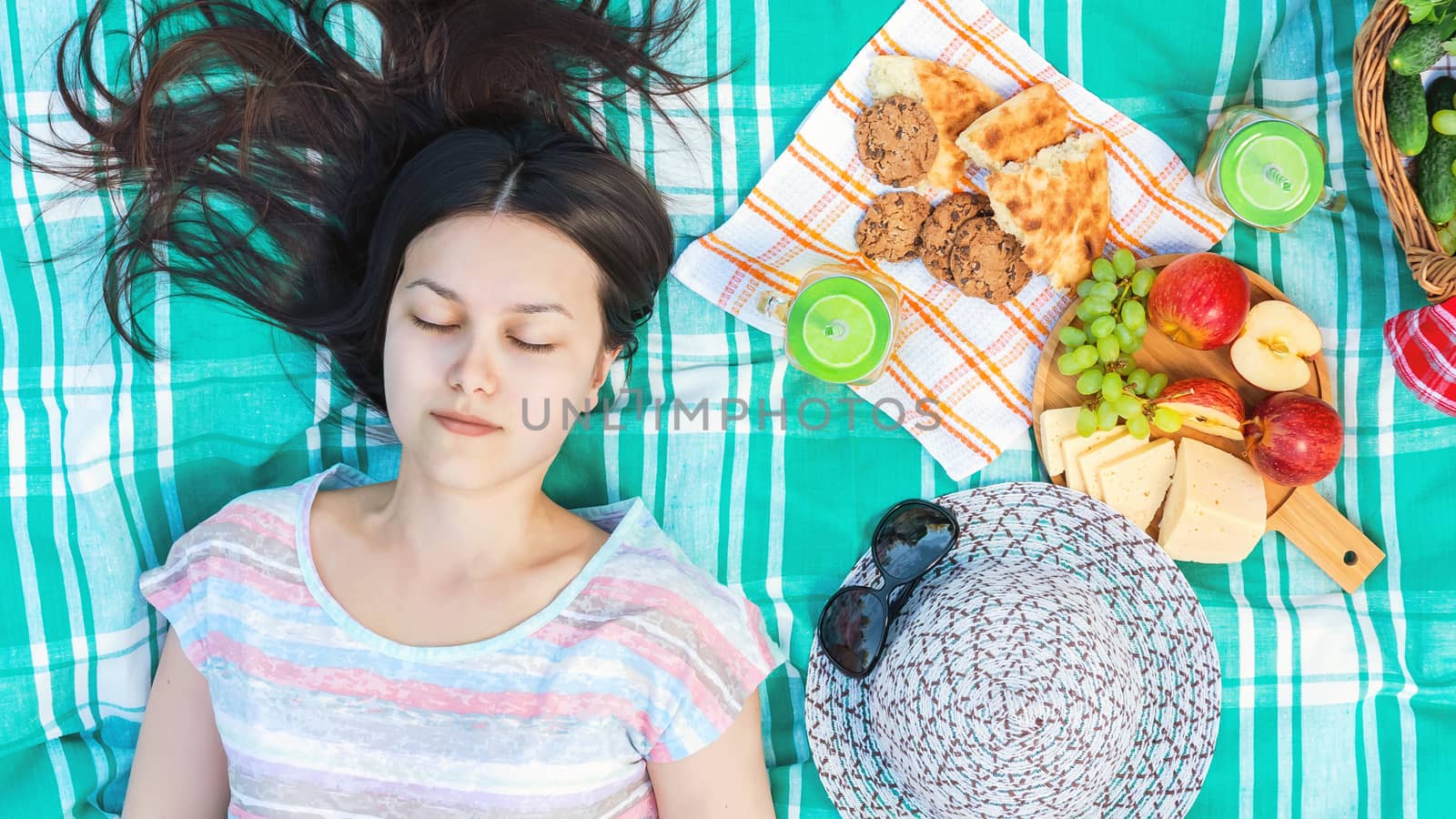 Young girl with long dark hair is lying on a plaid on a picnic on a summer day - summer holidays and vacation concept.
