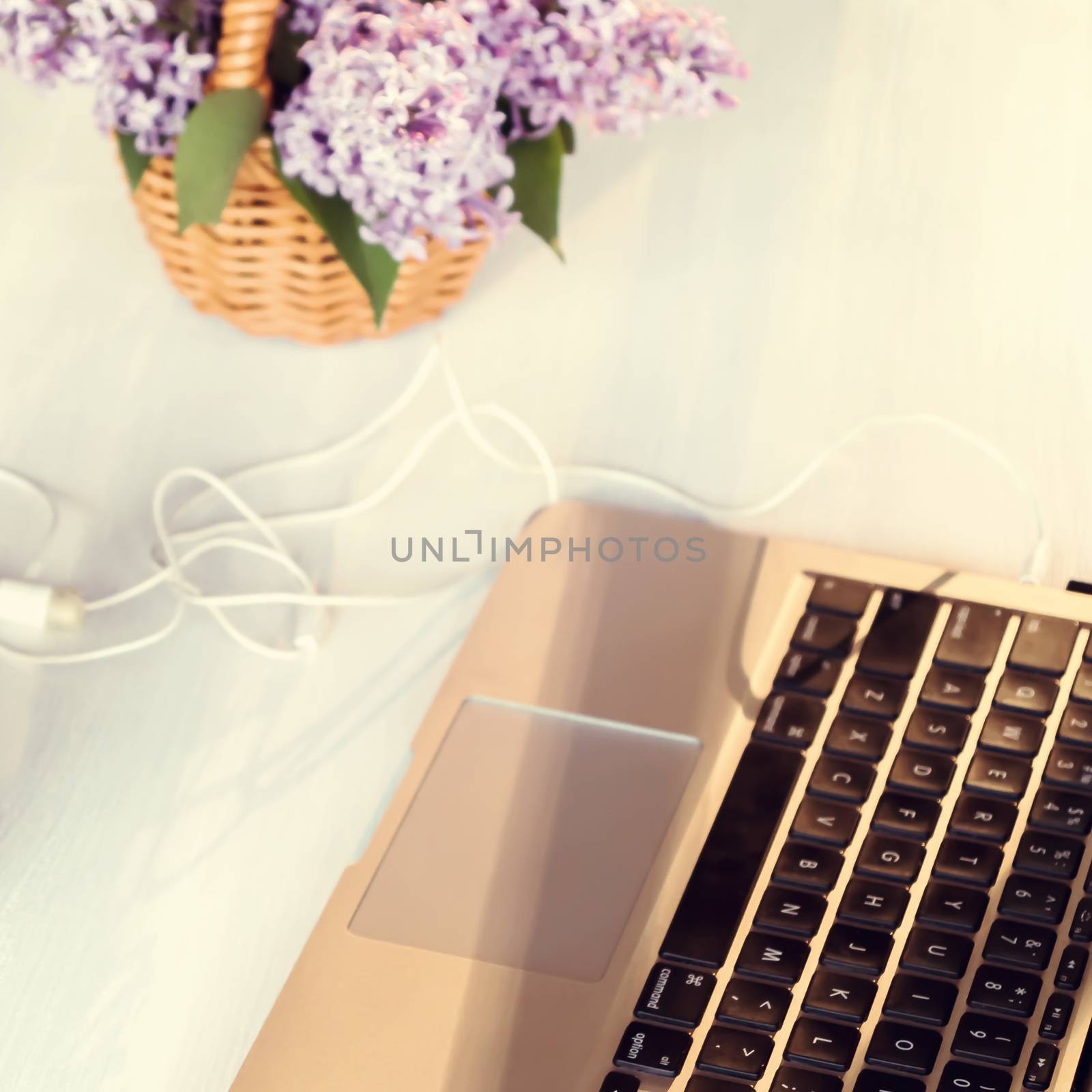 Laptop and a basket of lilac flowers on a white wooden table in the summer terrace - concept of remote work, online business, self-employment.