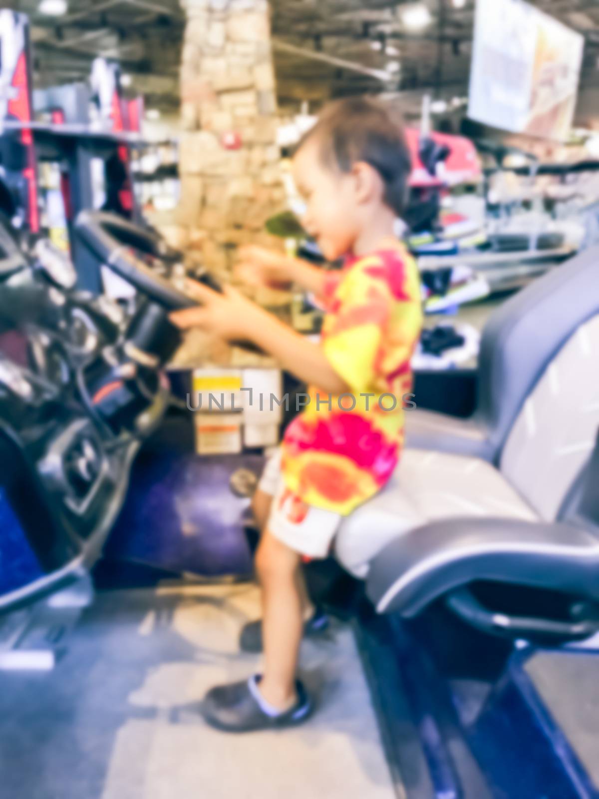 Abstract blurred Asian toddler boy try driving the boat at showroom large outdoor store in Texas, America. Boat buying and servicing concept