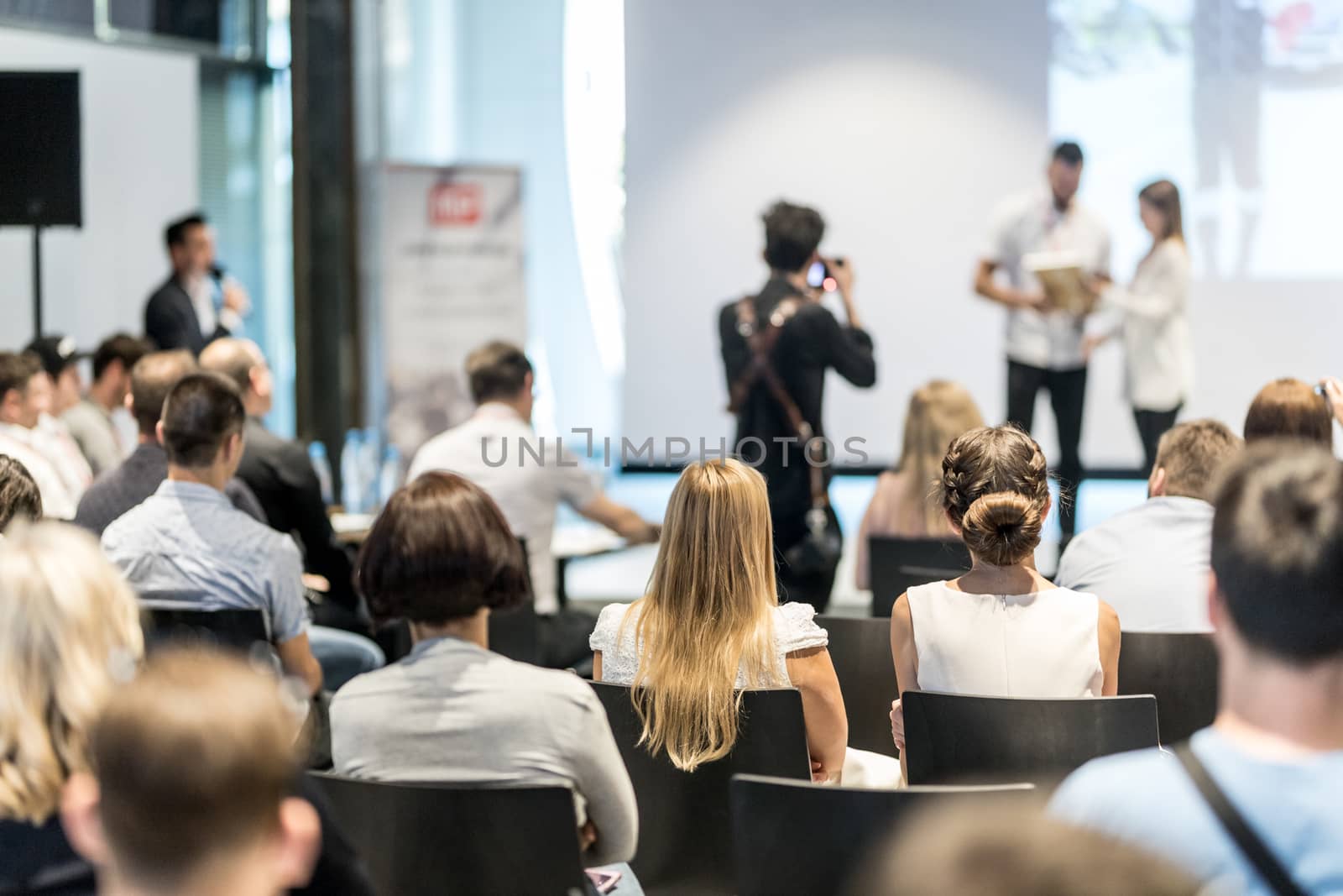 Young business team receiving award prize at best business project competition event. Business and entrepreneurship award ceremony theme. Focus on unrecognizable people in audience.