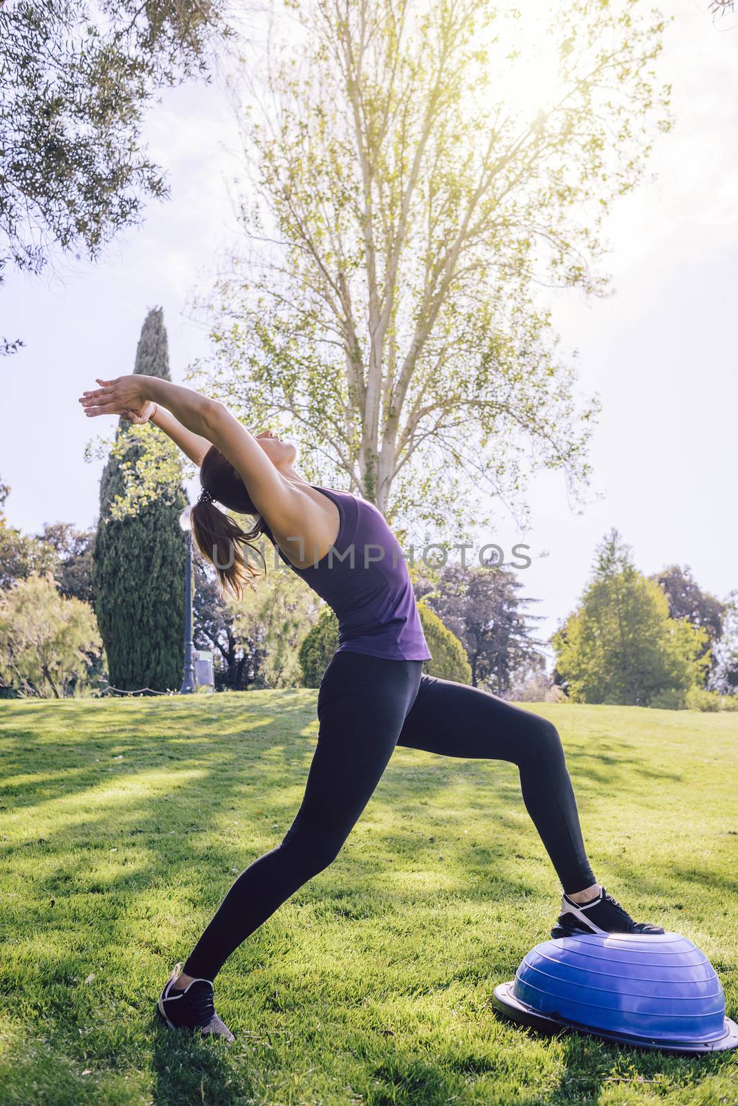 vertical photo of a healthy young female doing stretching yoga workout on the grass on a sunny day, she is outdoors in a park at the morning