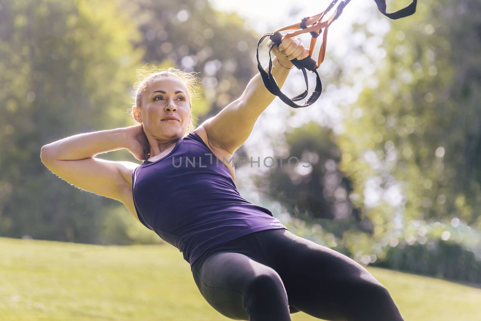attractive young woman training fitness with suspension straps, during functional workout in a sunny outdoor park in the morning