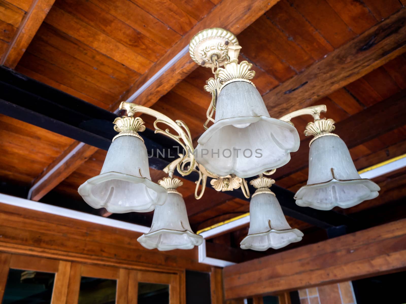 beautiful vintage interior background of a lighted retro chandelier hanging on a wooden ceiling, decorated lamp with flowers