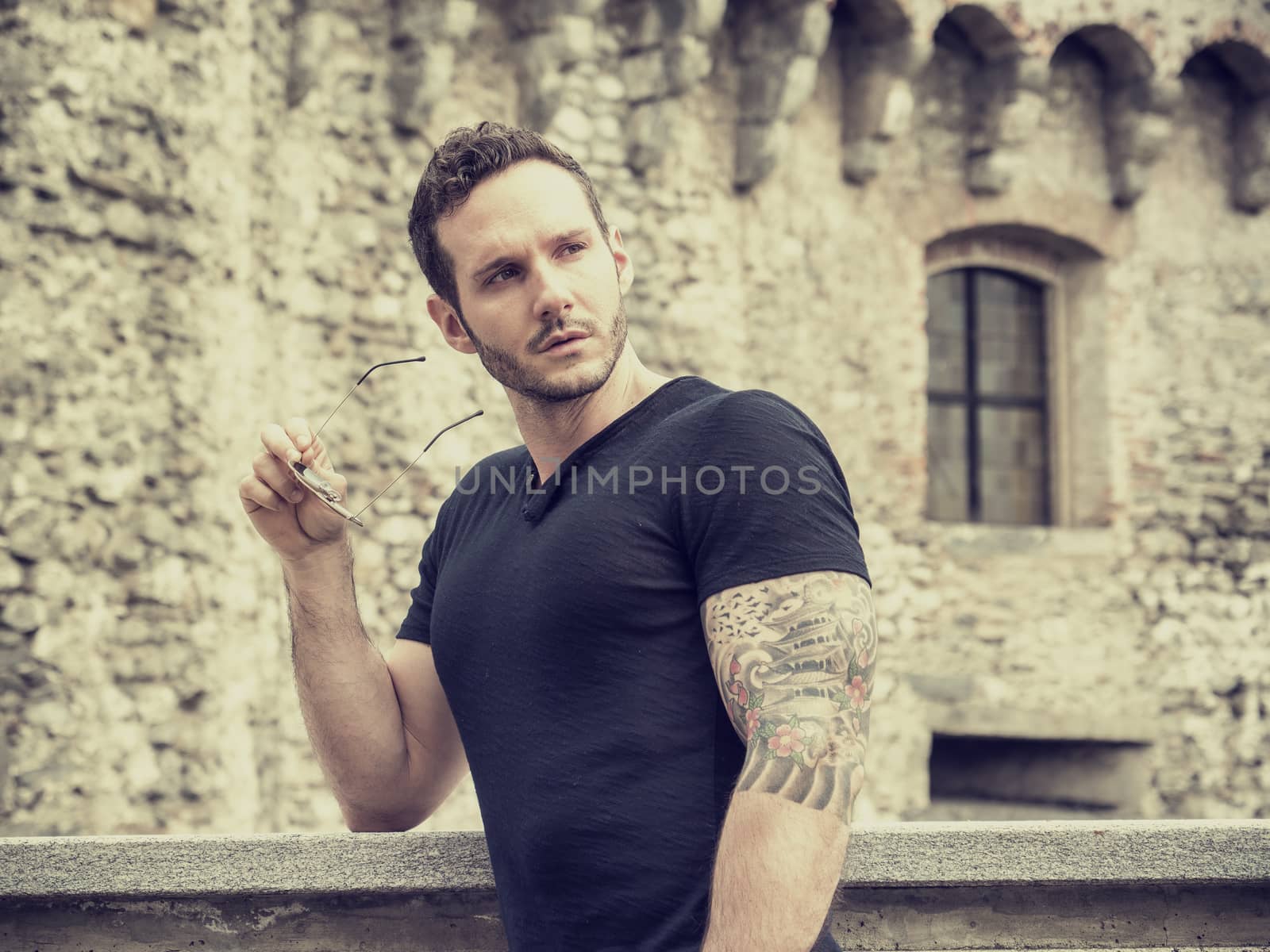 Attractive man outdoor in old European castle, in Switzerland. Athletic build, with tight t-shirt and sunglasses