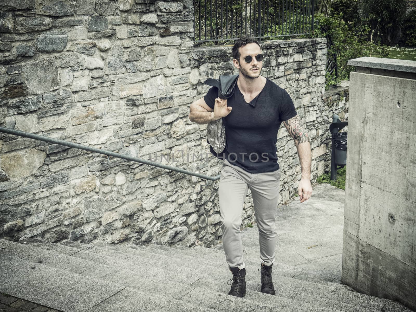 Attractive man outdoor in old European castle, in Switzerland. Athletic build, with tight t-shirt and sunglasses