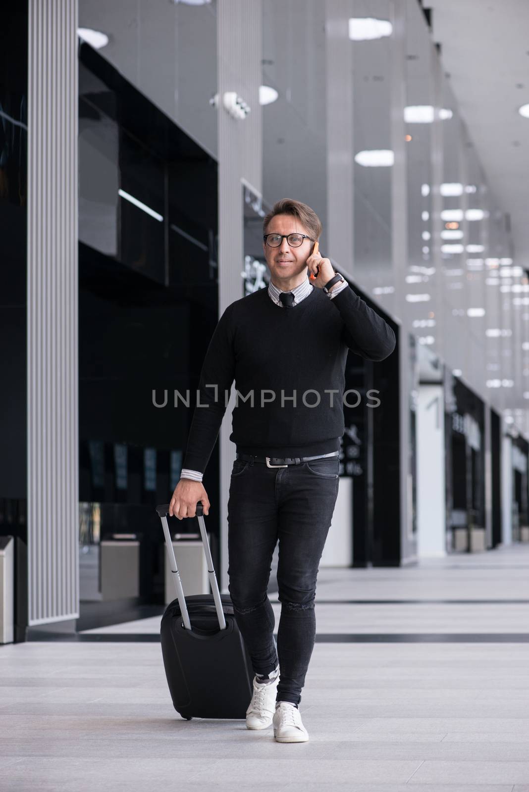 Man walking with wheeled bag at airport terminal and talking on phone