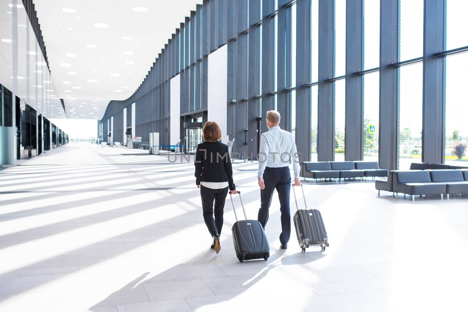 Business people in formal clothing walking with wheeled bags at airport terminal