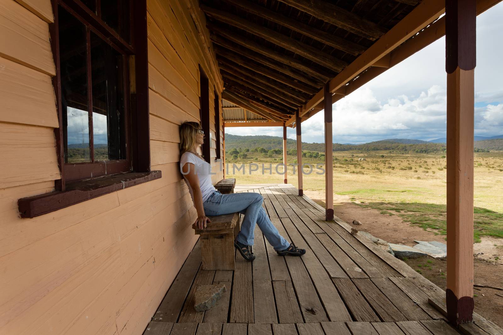 Woman relaxing on the rustic timber bench on the timber plank verandah of rural homestead in the beautiful Snowy High Plains Kosciuszko. A storm is brewing in the late afternoon. Rural lifestyle