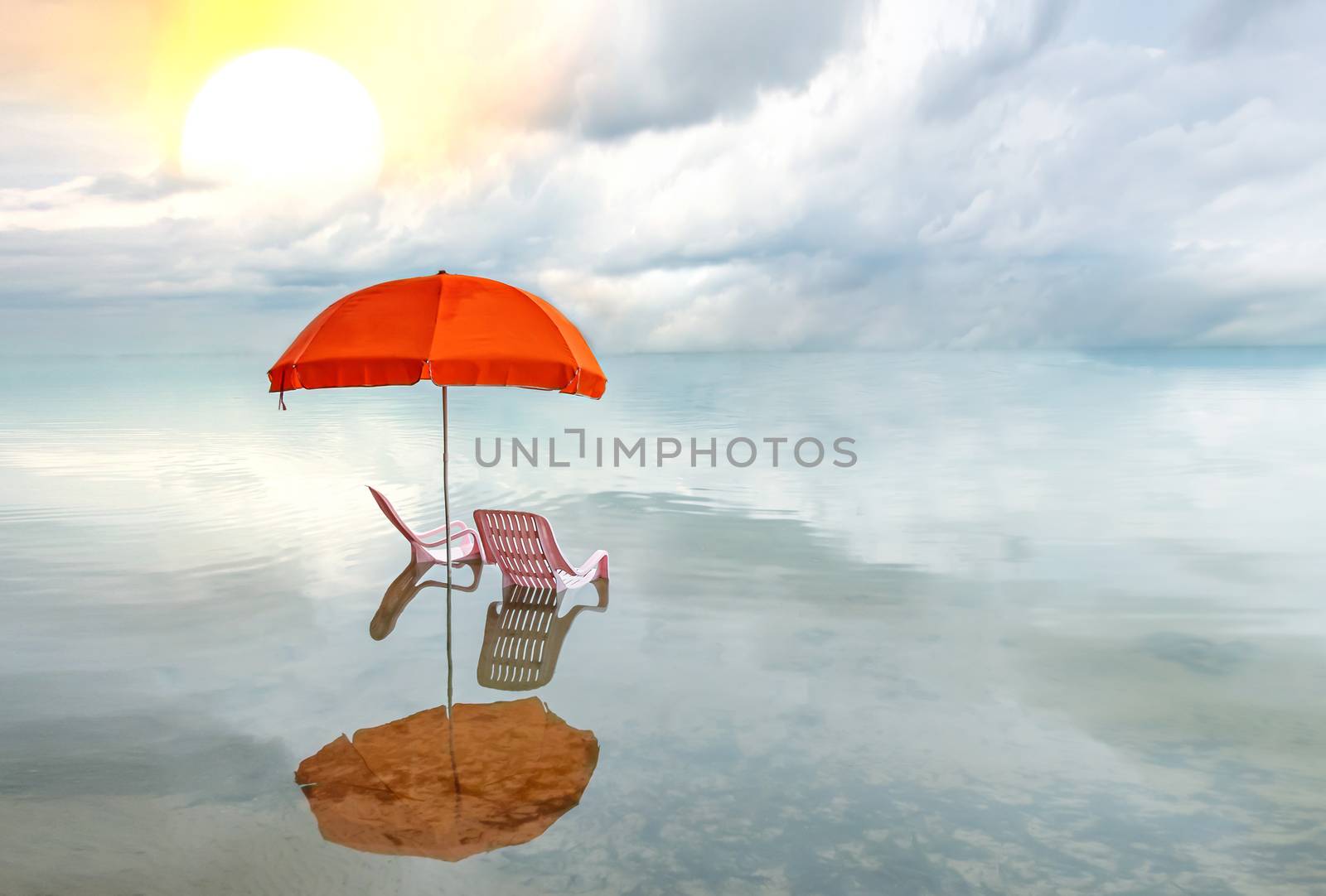 Two pink lounge chairs with  sun umbrella in a sea