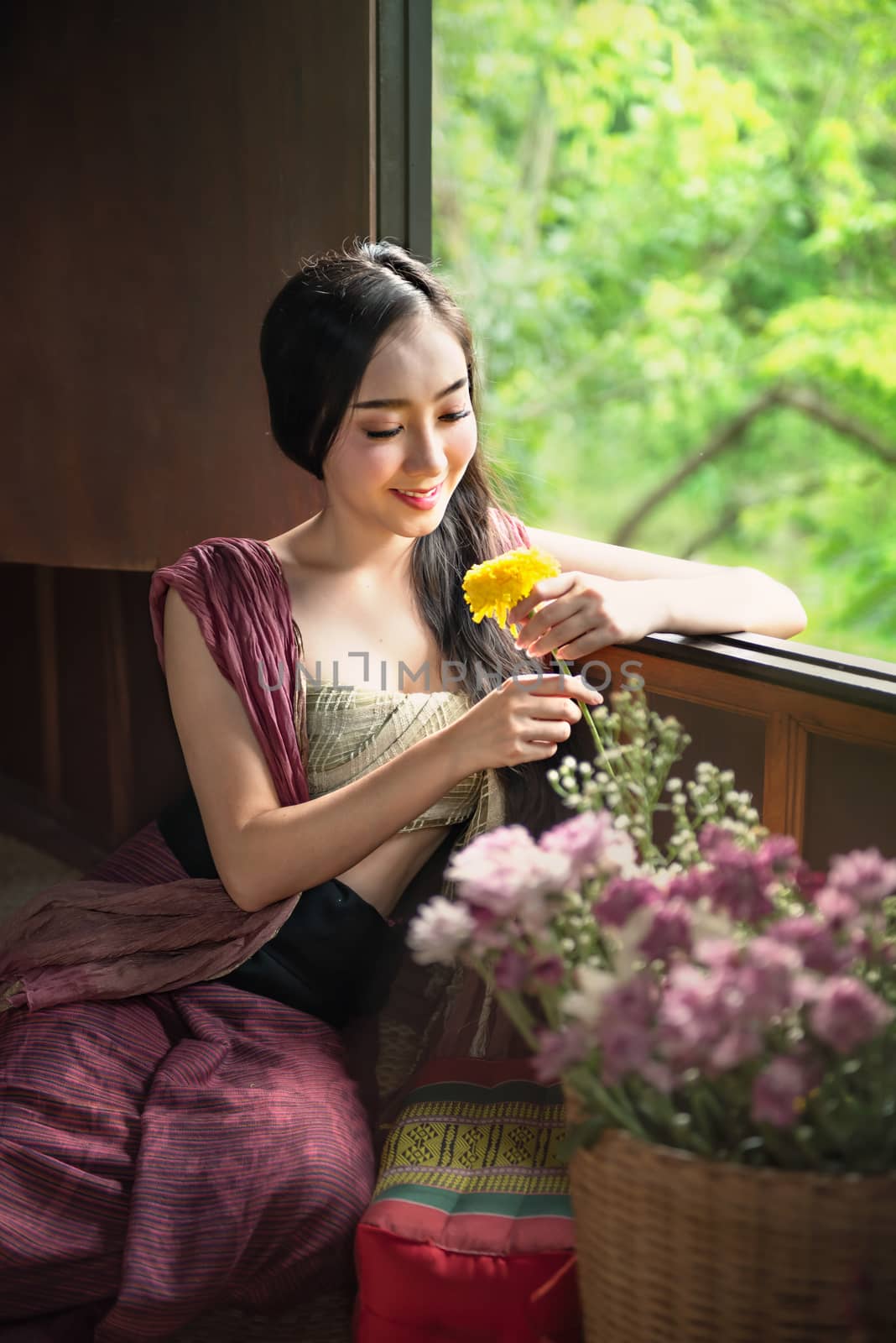 beautiful woman in traditional asian dresses holding flowers sitting near the windows