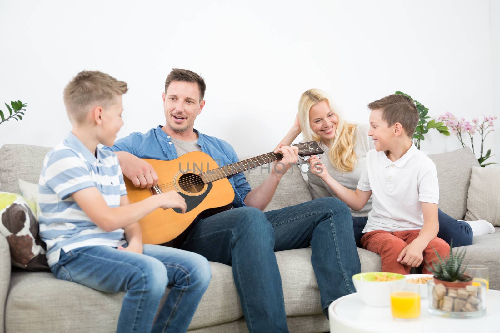 Happy caucasian family smiling while playing guitar and singing songs together at cosy modern home. Spending quality leisure time with children and family concept.