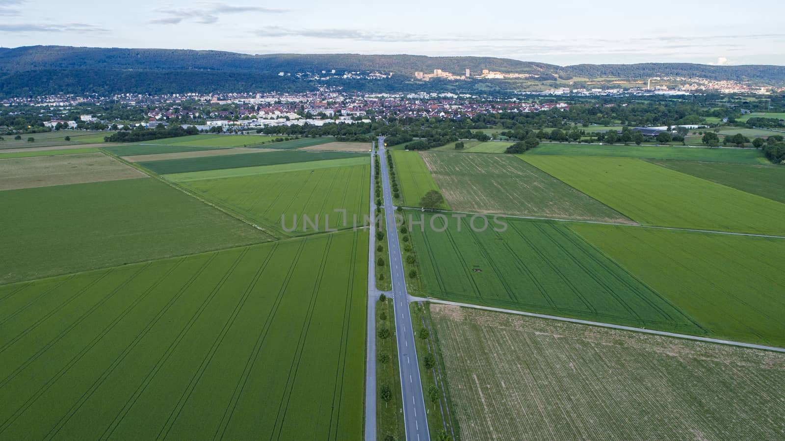 Aerial Capture of Countryside Landscape with Long Empty Road and City in Background by CristianDina