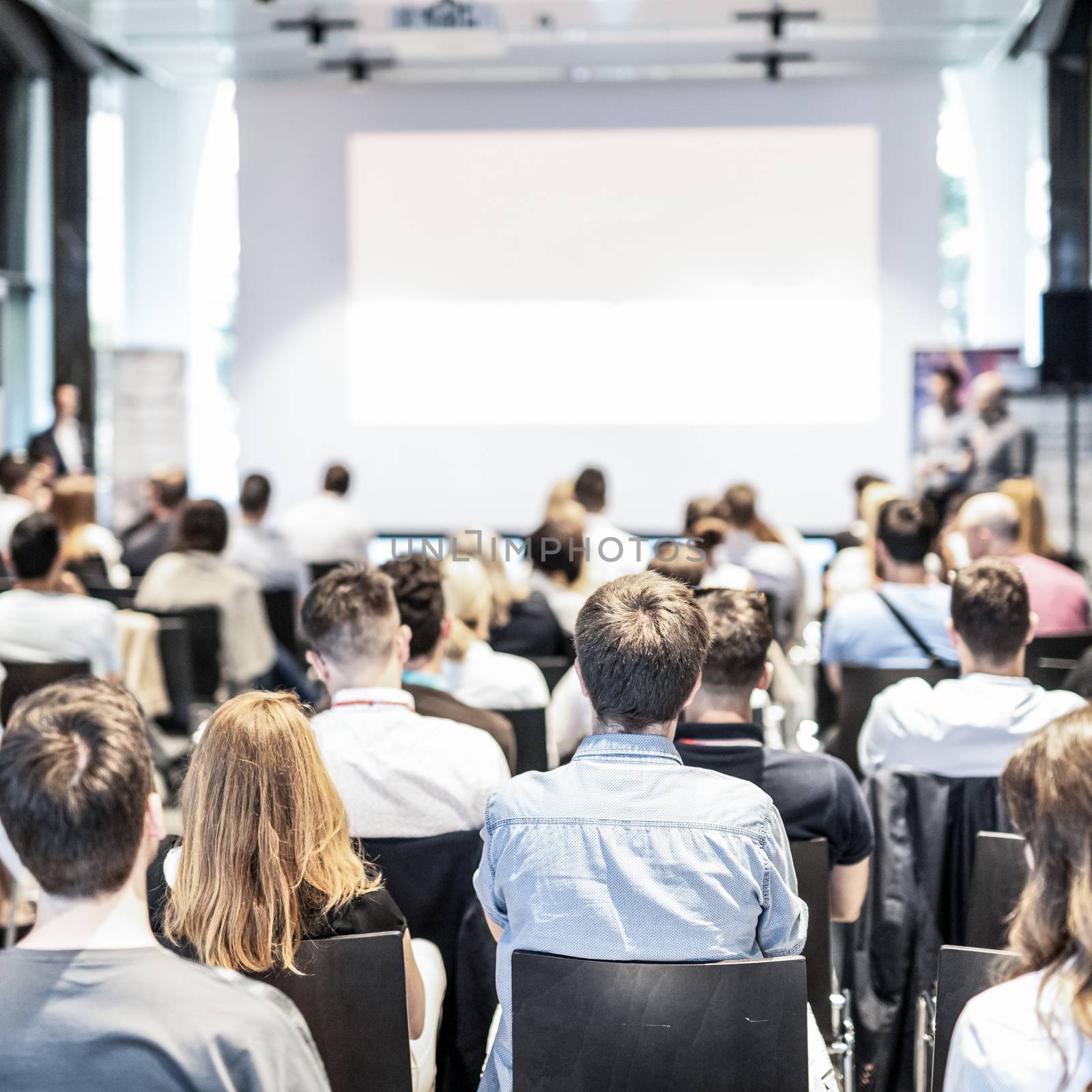 Audience at the conference hall. Copy space on the white screen. Talk at business conference event. Business and Entrepreneurship concept. Focus on unrecognizable people in audience.