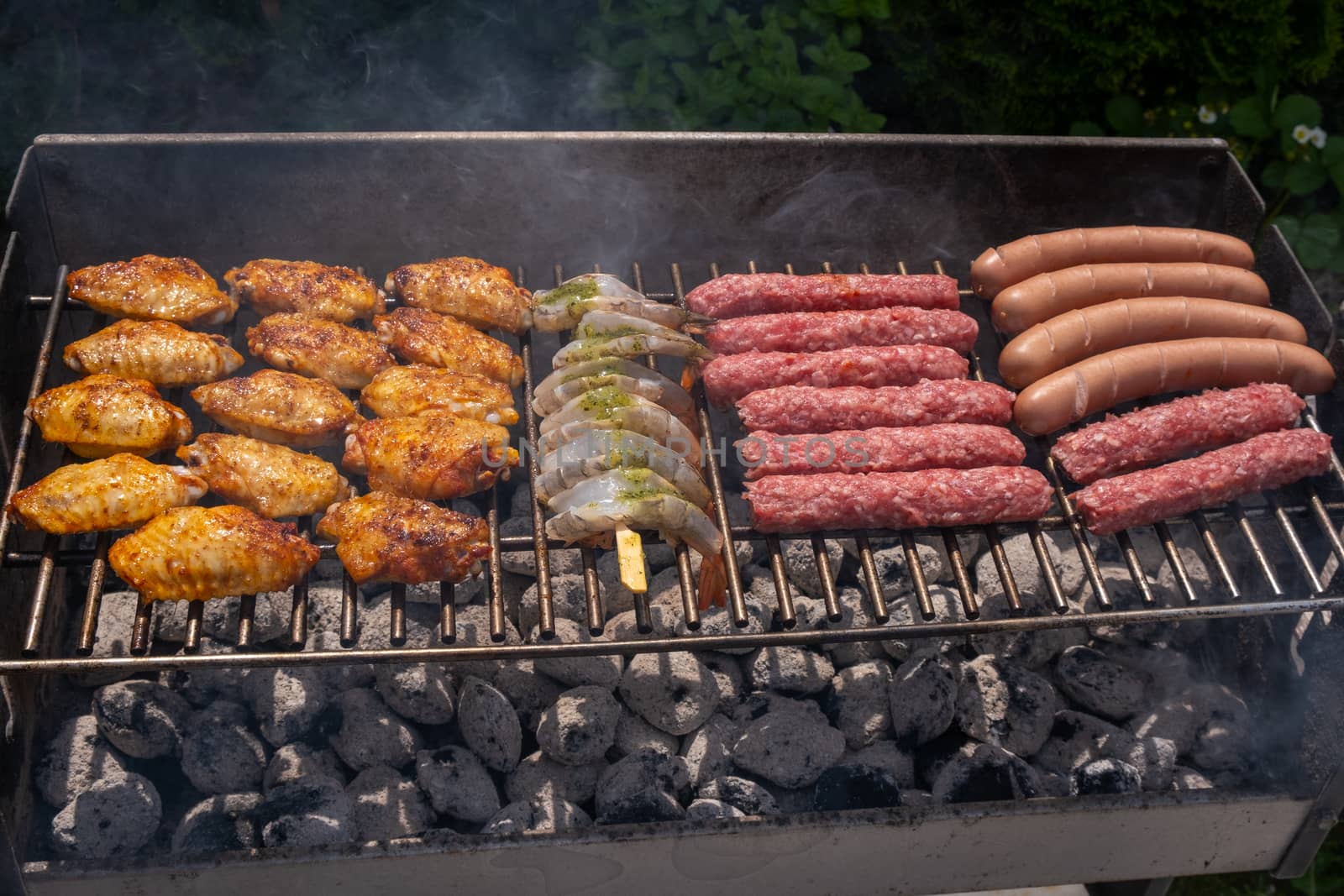 Mixed assortment of marinated meat, chicken, and prawns grilling on hot coals on a BBQ by asafaric