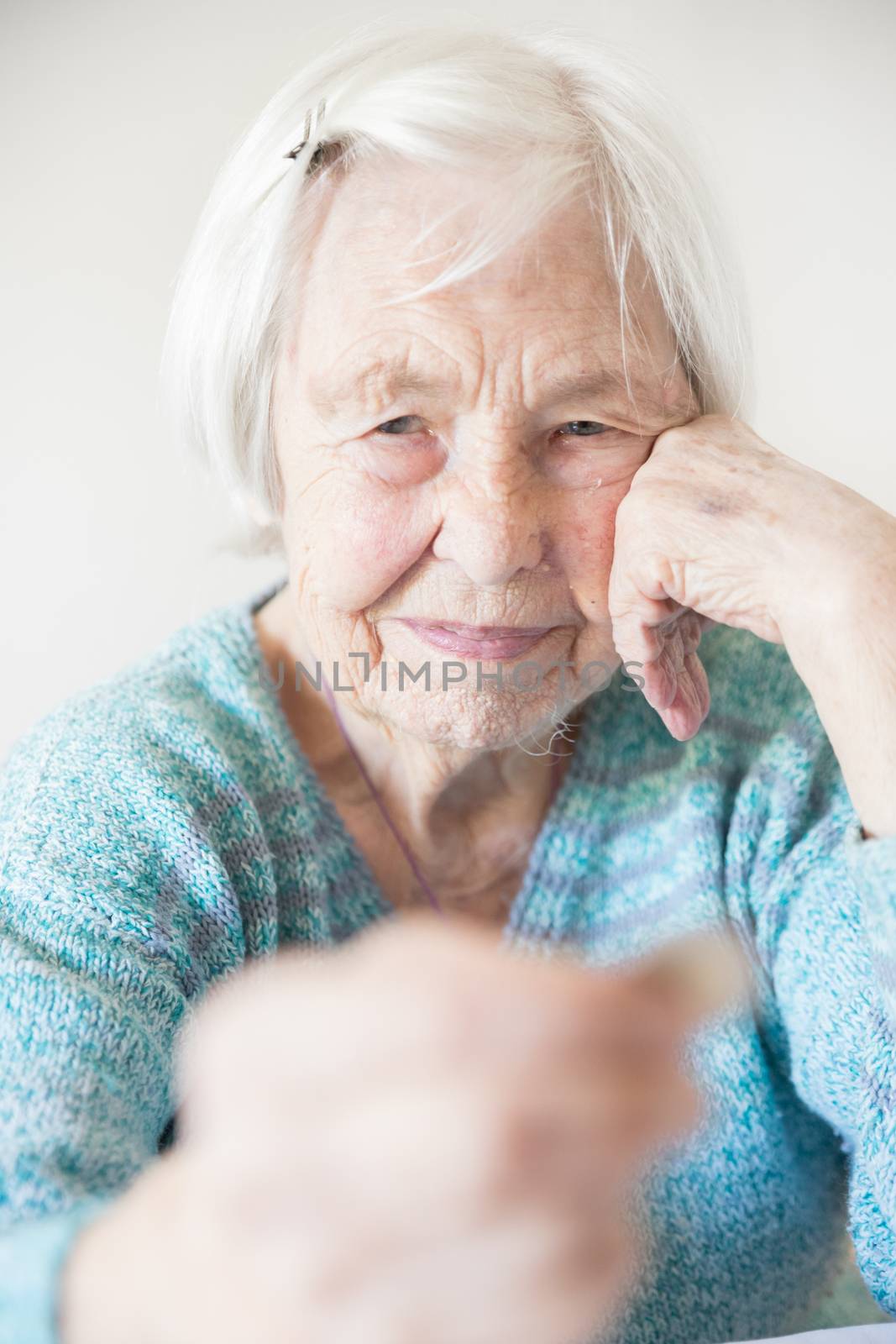 Sad elderly woman sitting at the table at home and looking miserably at only remaining coin from pension in her hand. Unsustainability of social transfers and pension system. Selective focus image.