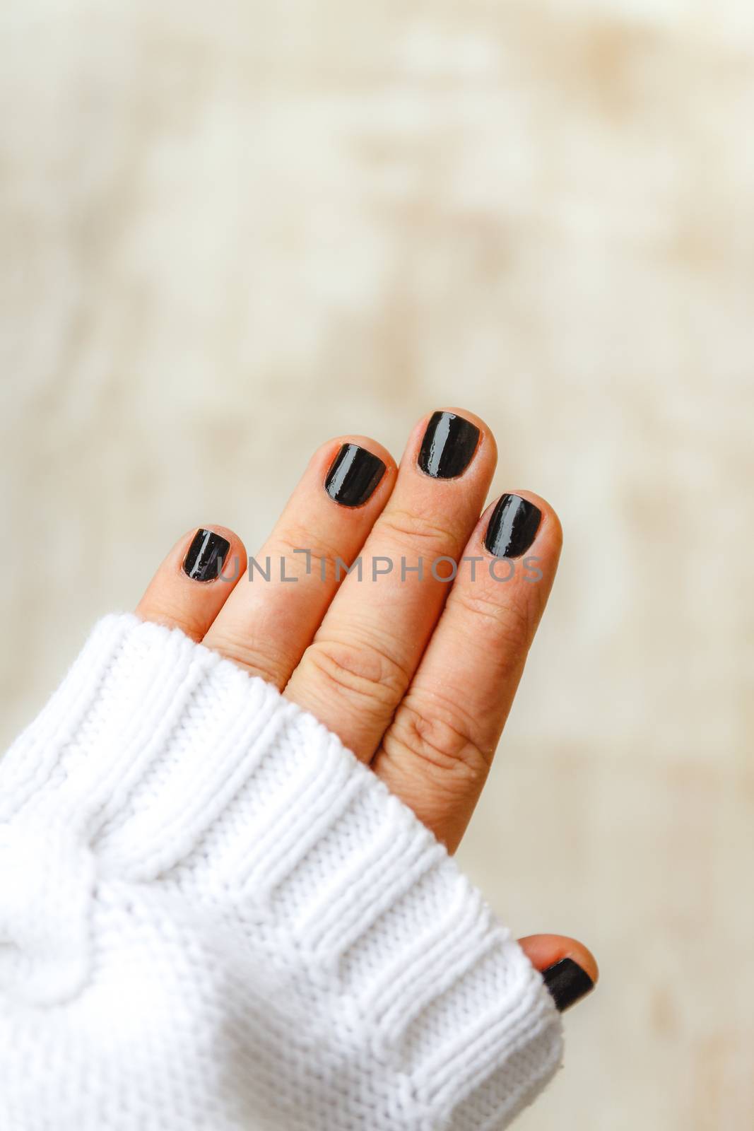 hand with black manicure on short nails in a white sweater on a  by Tanacha
