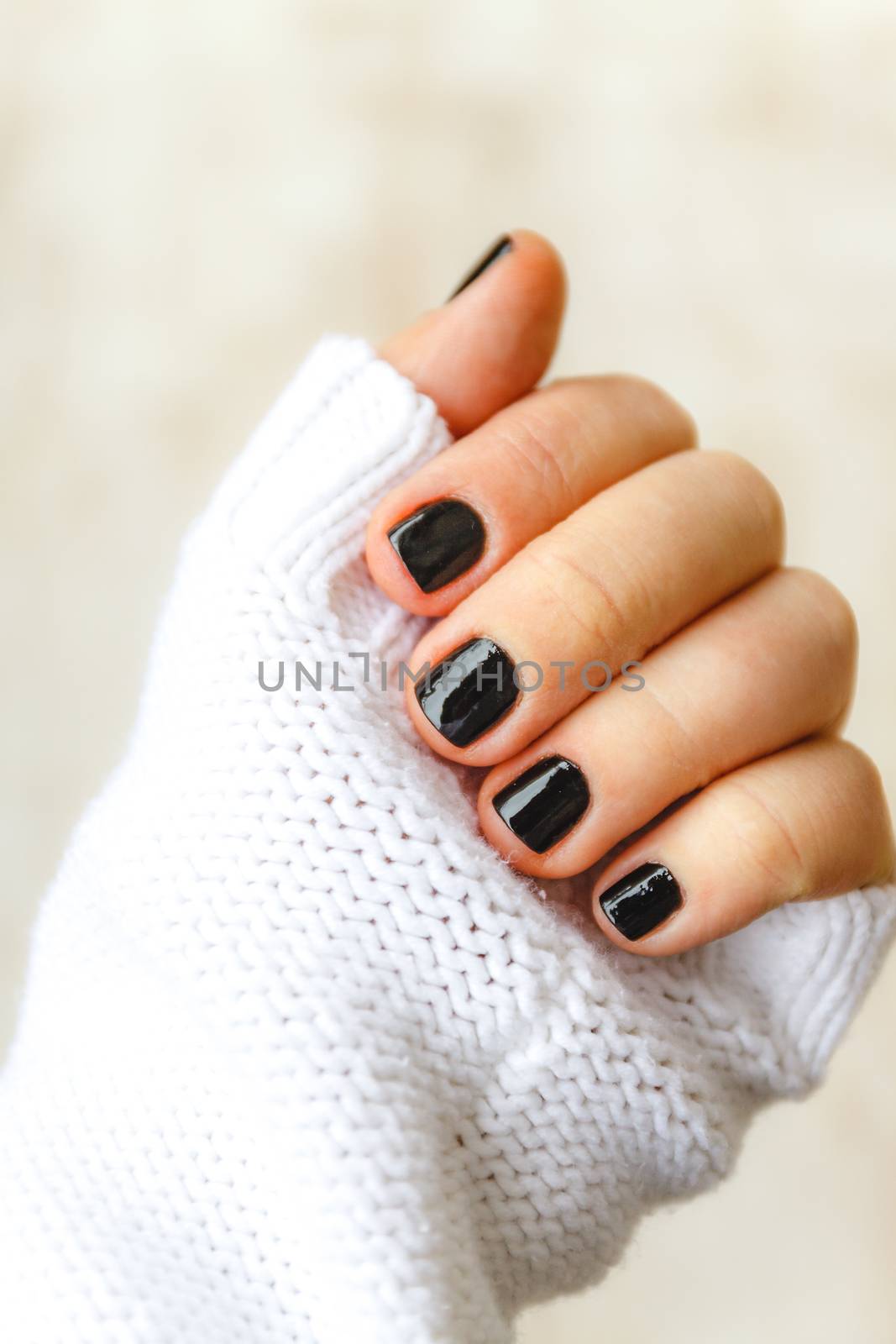 hand with black manicure on short nails in a white sweater on a light background. The concept of a stylish and warm winter.
