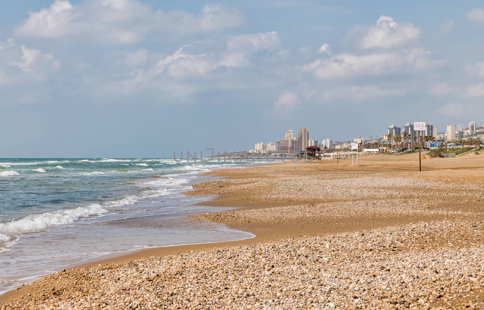 the haifa beach in israel with the city as background and a raw sea with waves at the coastline