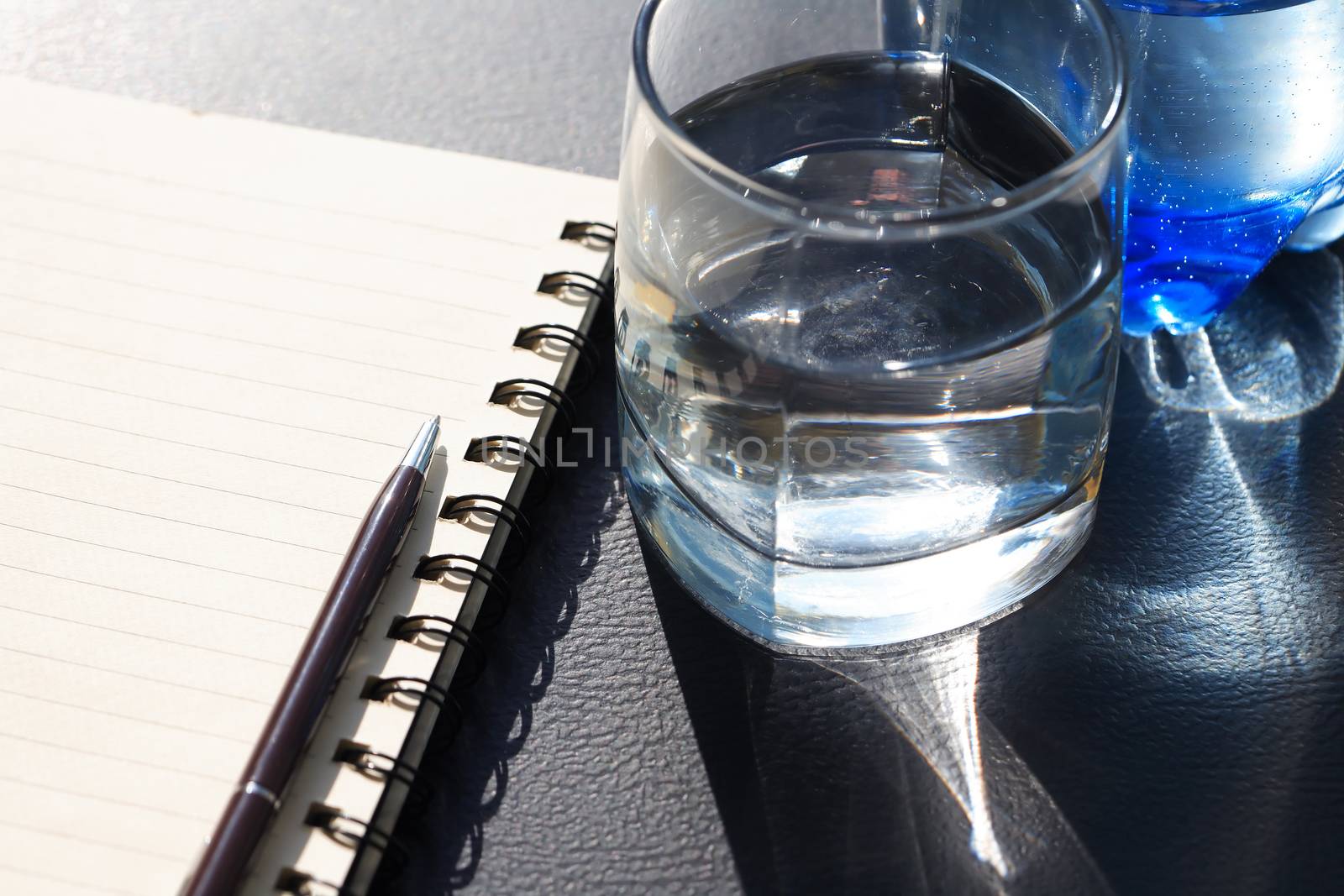 Glass of water near pen lying on open notepad