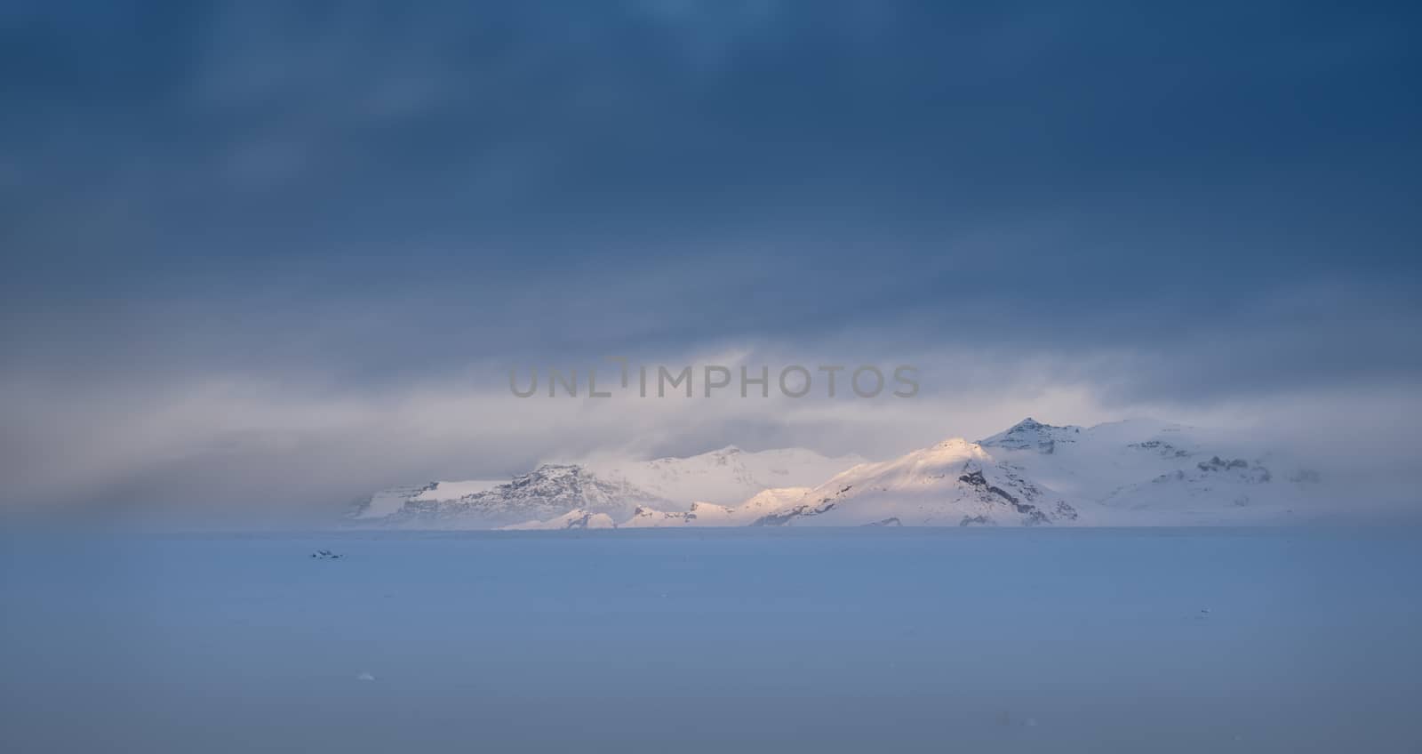 Focssed morning sunshine on a mounting range, winter day in Iceland with overcast sky and snow-covered land