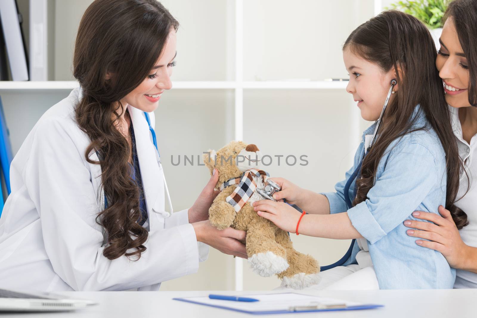 Happy mother and child with teddy bear and stethoscope at pediatrician office