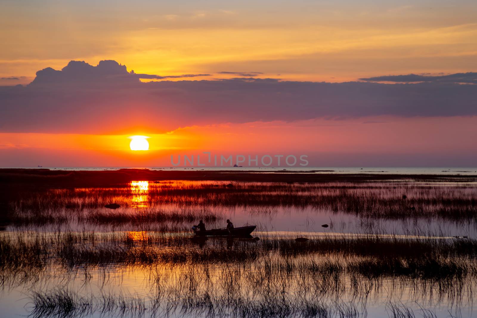 Silhouette of a fishing boat on the lake against the background of a beautiful sunset sky reflected in the water. by Anelik