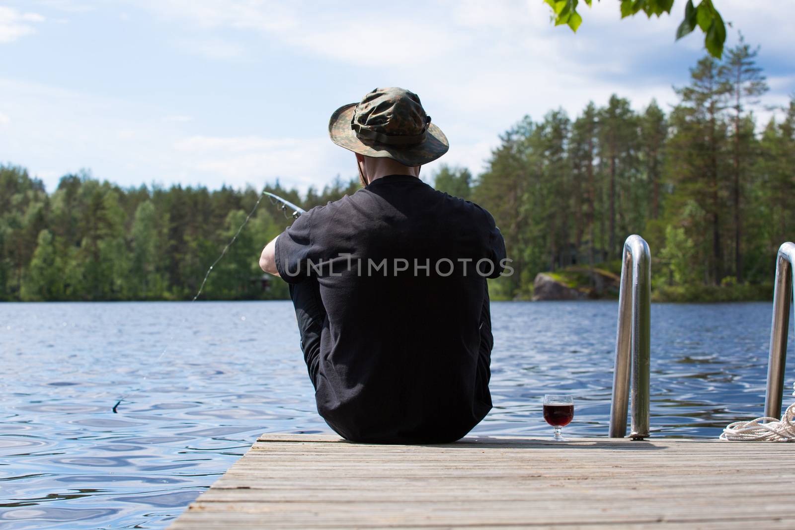 Mature man fishing from wooden pier near cottage on lake in Finland at summer