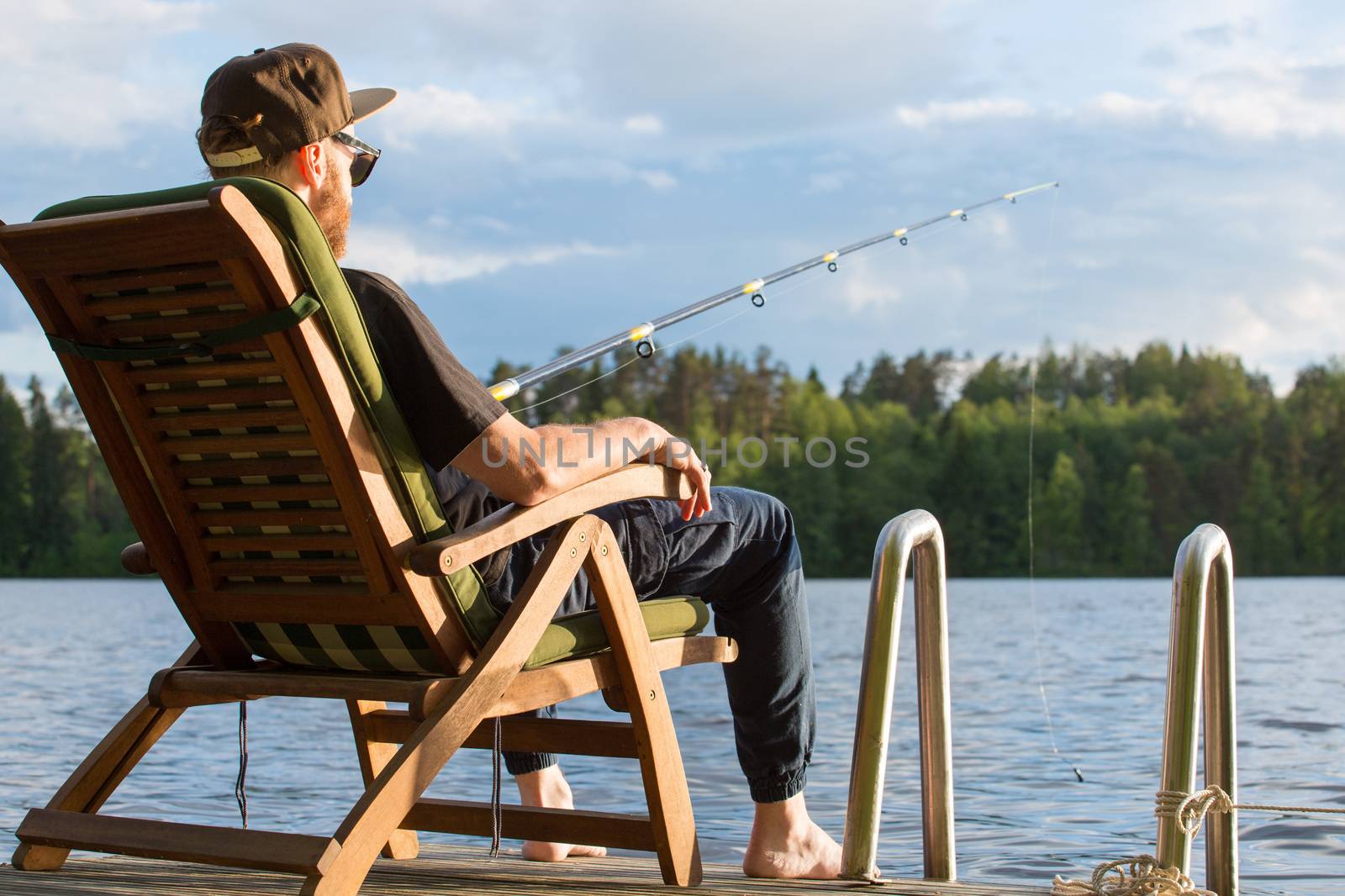 Mature man fishing from wooden pier near cottage on lake in Finland at summer