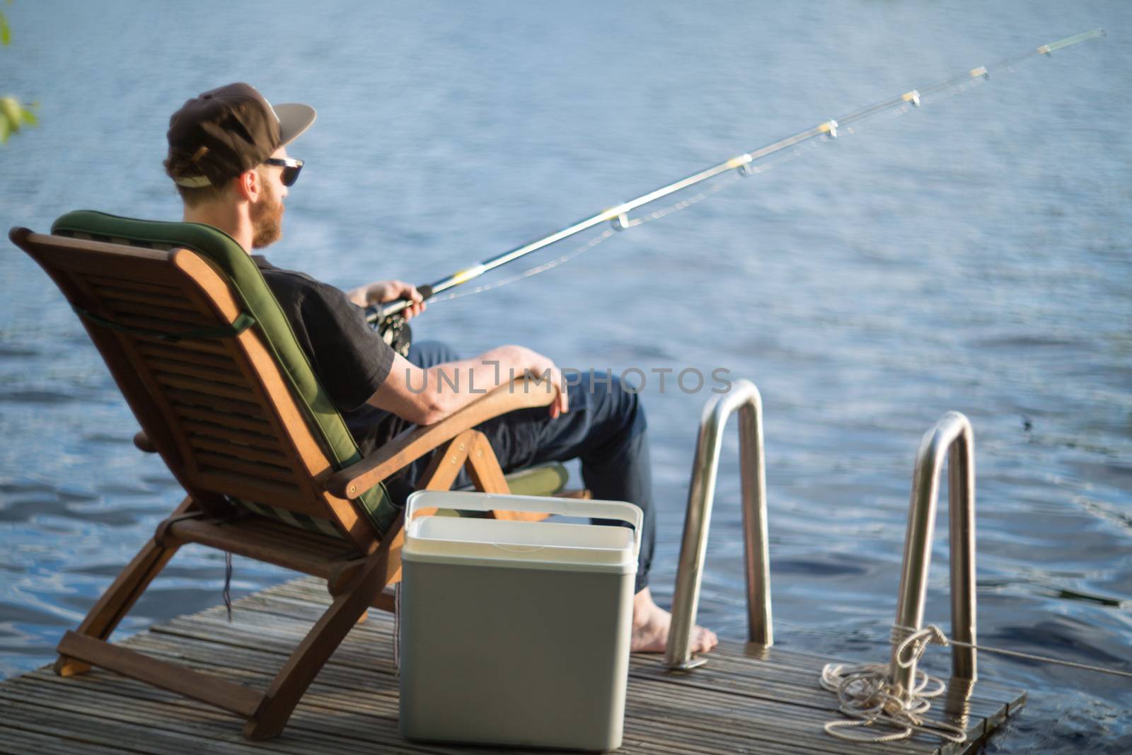 Mature man fishing from wooden pier near cottage on lake in Finland at summer