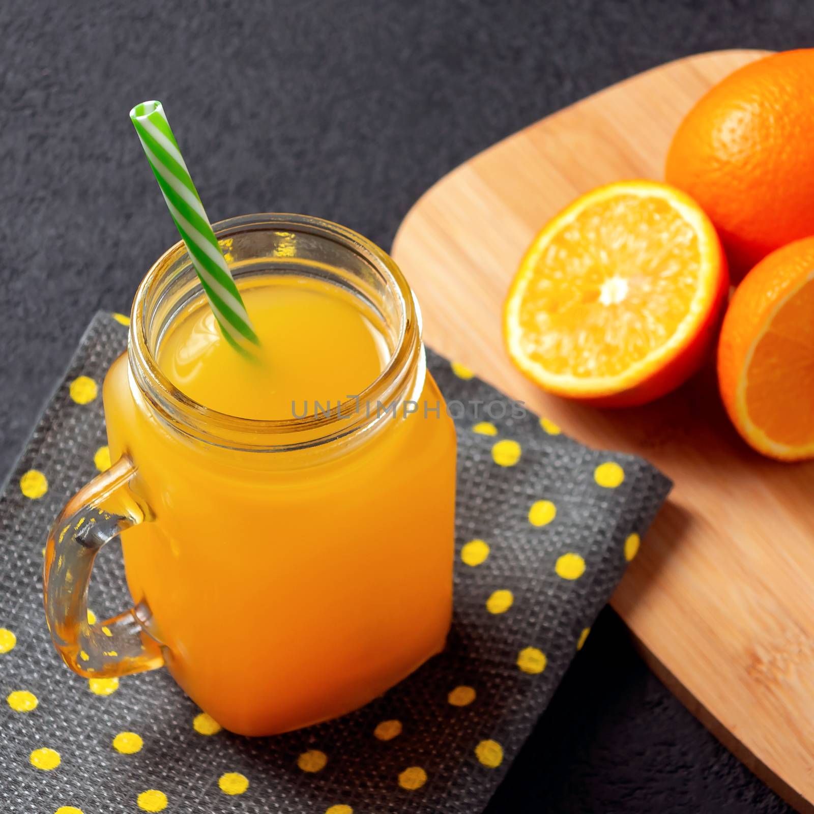 Freshly made citrus juice from oranges, grapefruit and lime in a jar-mug with a straw on black table by galsand