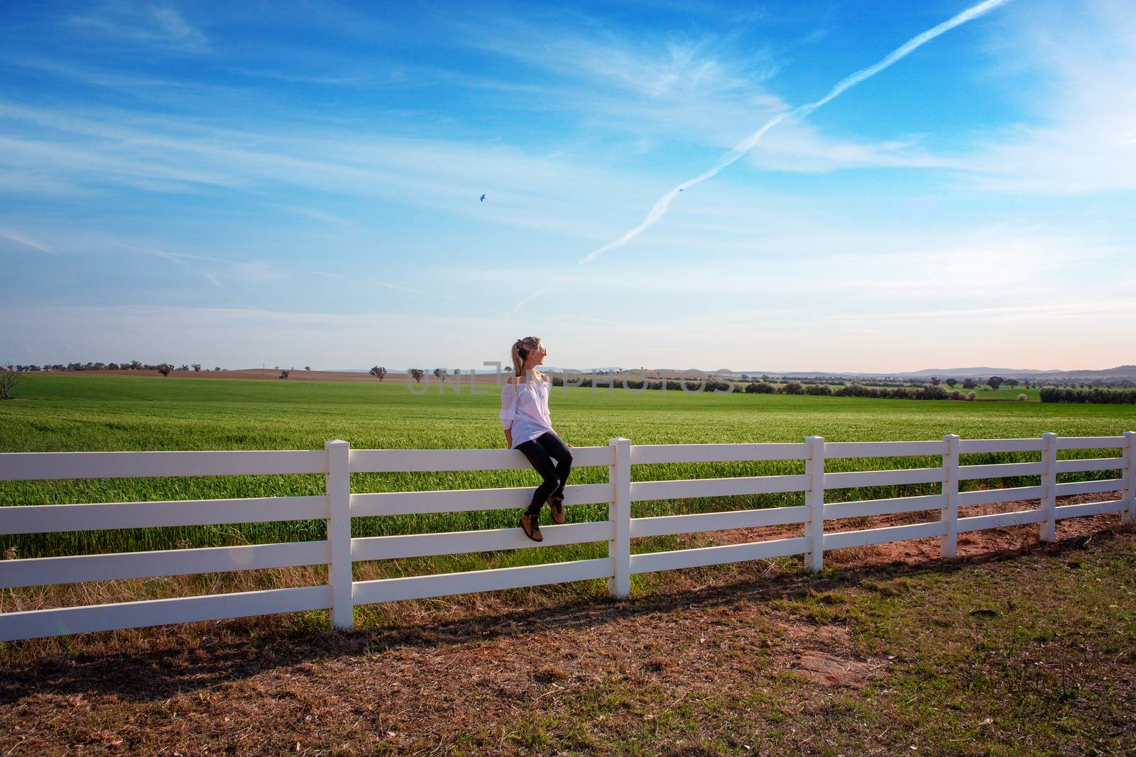Woman sitting on white farm fence in rural fields by lovleah