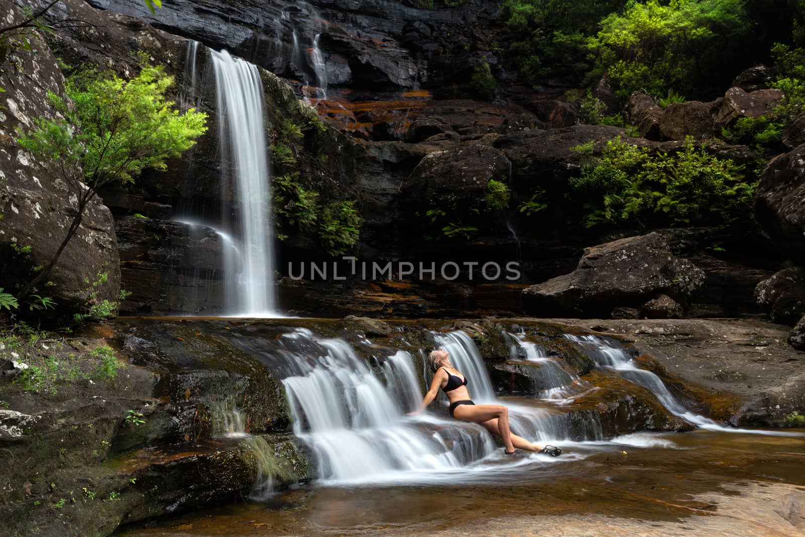 Woman sitting in flowing waterfall cascades immersed in nature oasis by lovleah