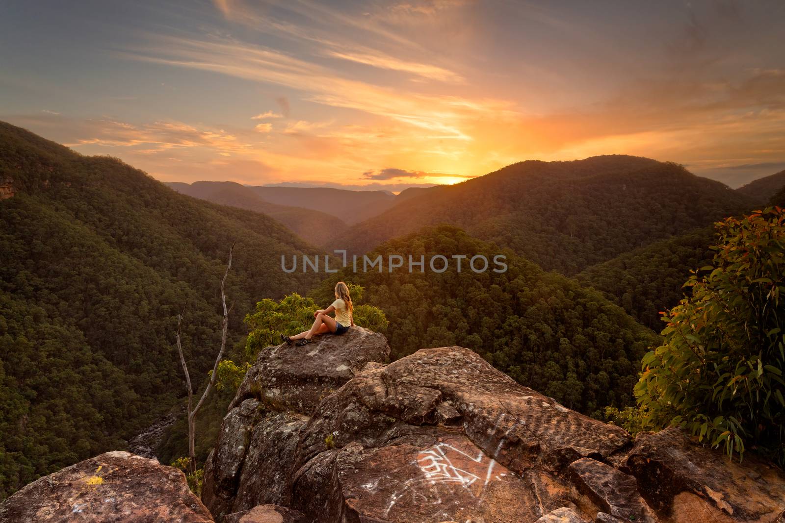 A female relaxes on a rock with stunning wilderness valley views westwards towards the beautiful sunset.  Blue Mountains Australia